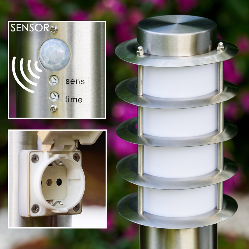 Metall-Außenlampe mit Sensor und Steckdose. Die Lampe hat vier weiße Lichtabschnitte. Hintergrund hat lila Blumen.