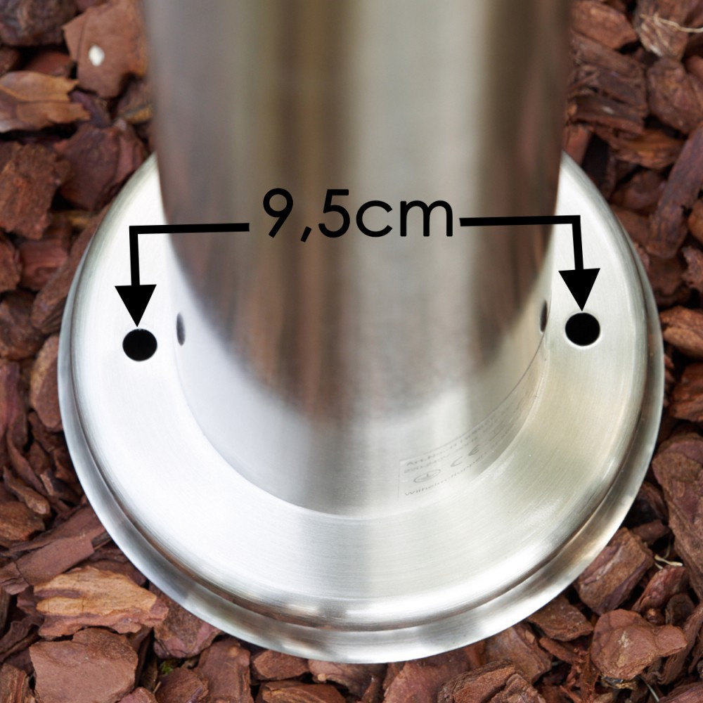 Ein Metallsockel mit zwei Löchern, 9,5 cm auseinander, liegt auf braunem Mulch. Eine Metallsäule ragt aus dem Sockel. Der Sockel hat ein kreisförmiges Design.