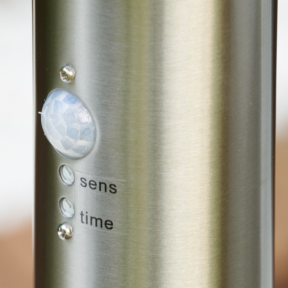 Nahaufnahme eines Objekts aus gebürstetem Metall mit Sensor, zwei Schrauben und den Beschriftungen 'sens' und 'time'.