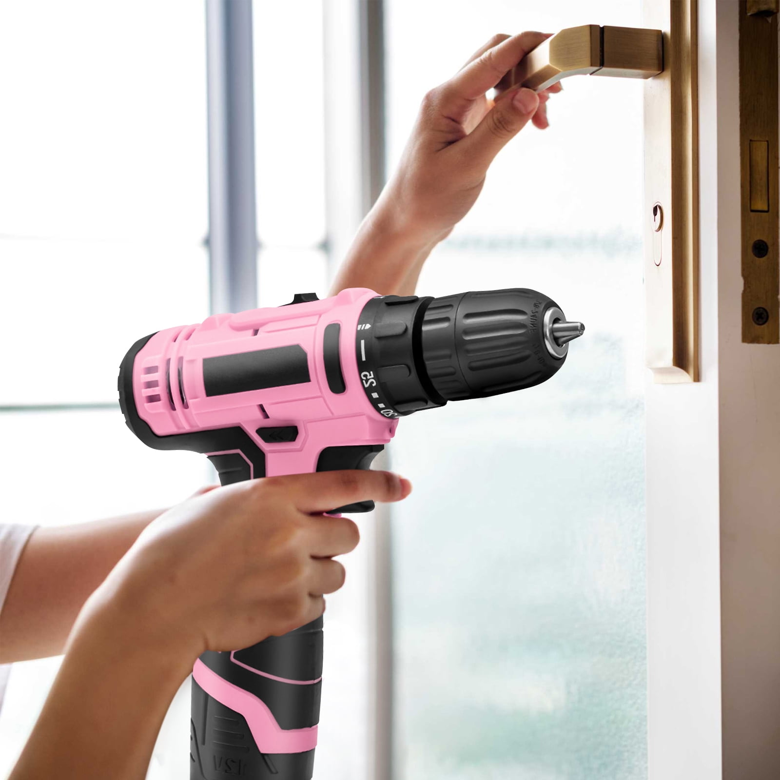 Eine Person benutzt einen pinkfarbenen und schwarzen Bohrer, um an einer Tür zu arbeiten. Eine Hand hält den Bohrer, die andere am Griff.