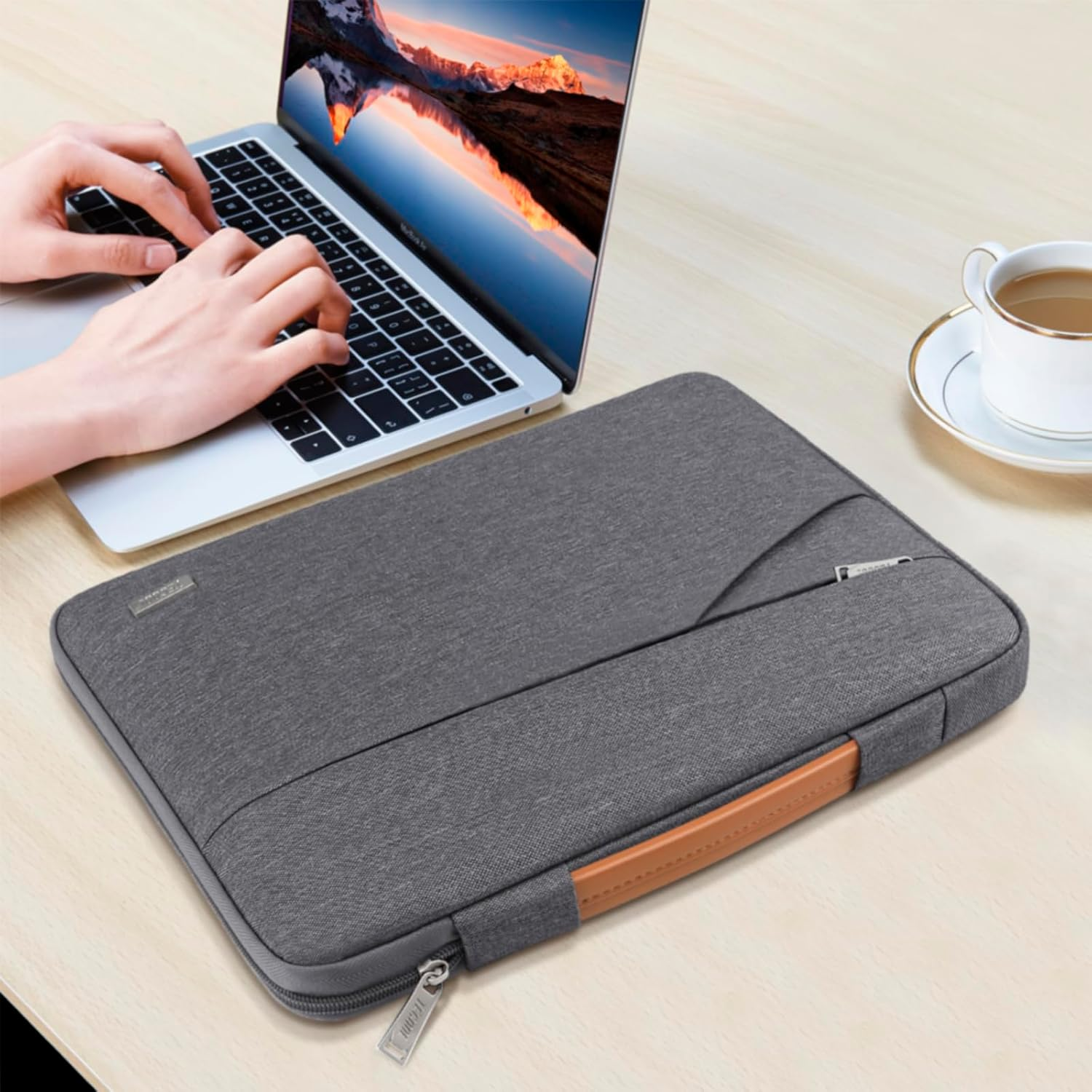 Eine Person tippt auf einem Laptop. Eine graue Laptop-Hülle und eine Tasse Kaffee liegen auf einem Holztisch.