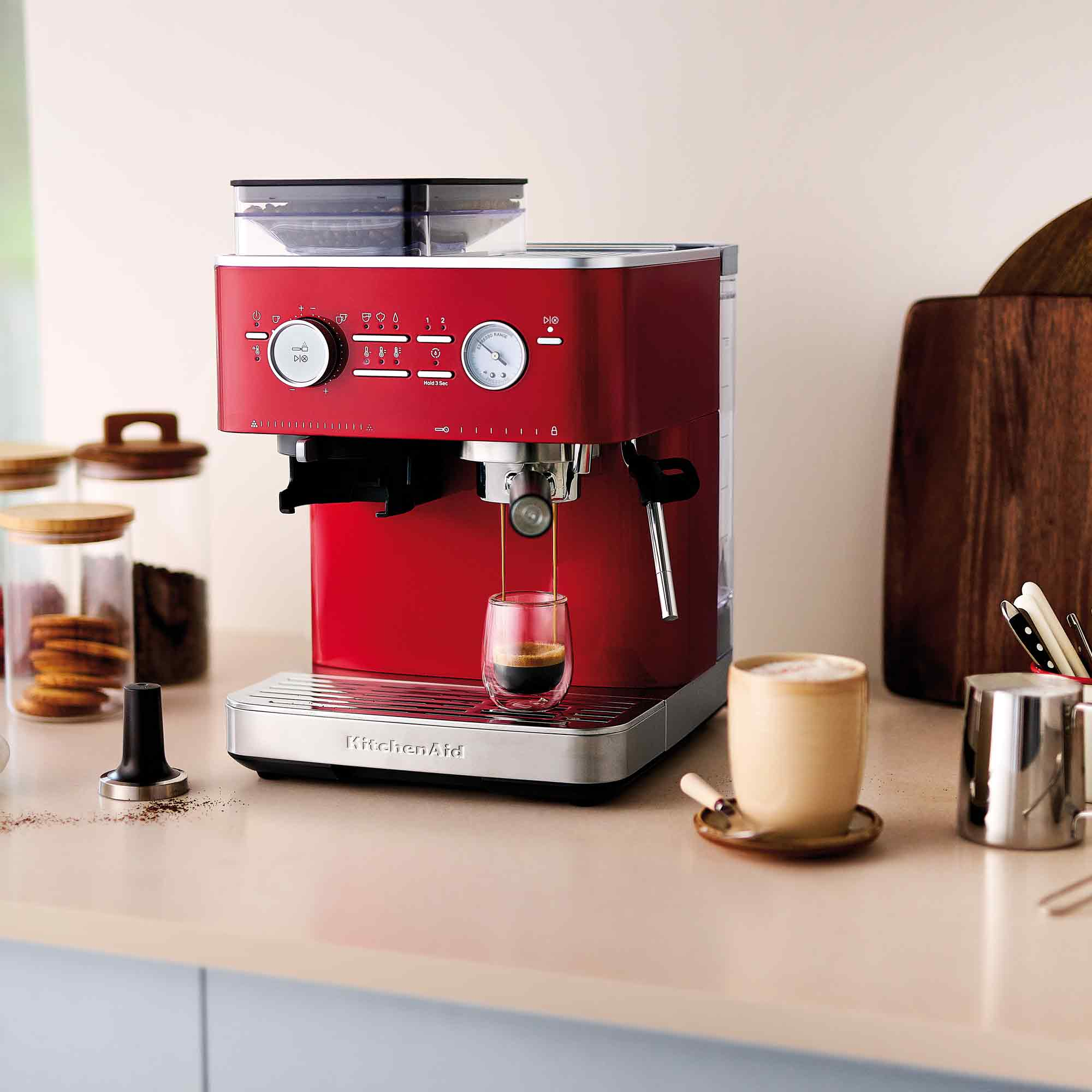 Rote Espressomaschine, die Kaffee in ein Glas gießt. Eine Tasse Kaffee und anderes Kaffeezubehör sind in der Nähe.