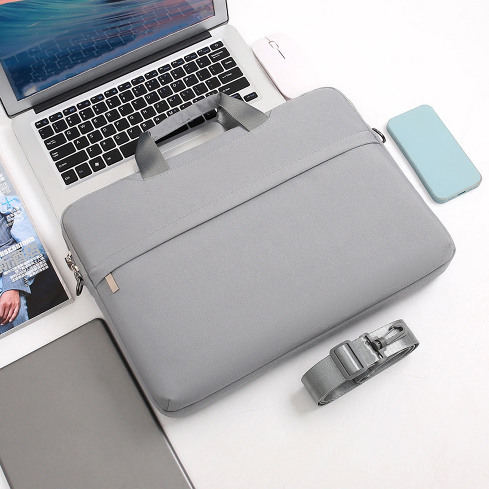 Graue Laptoptasche mit Griff, auf weißer Oberfläche mit Laptop, Maus, Telefon und Gurt.