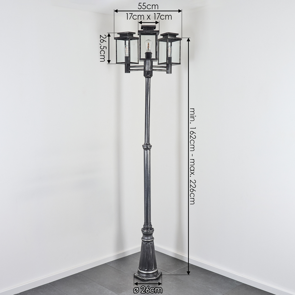 Eine hohe, schwarze Straßenlaterne mit drei Glaslaternen. Die Abmessungen werden neben der Lampe an einer weißen Wand und einem grauen Boden angezeigt.