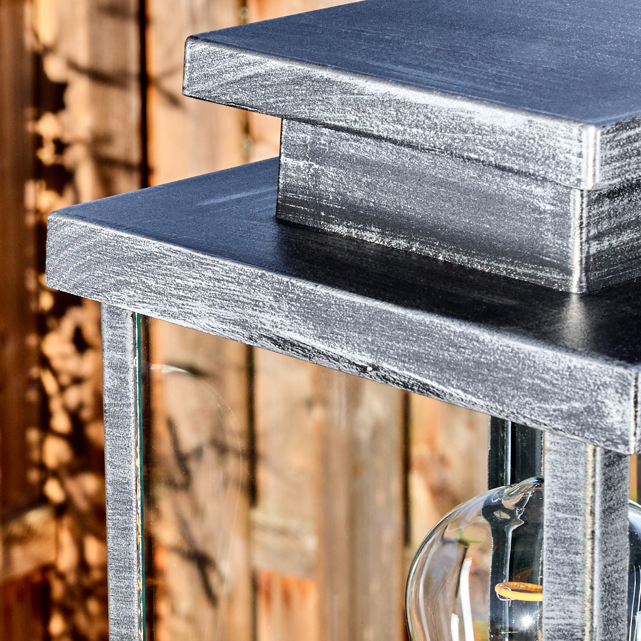 Nahaufnahme einer metallischen Laterne. Sie hat einen silbernen Rahmen, Glasscheiben und eine freiliegende Glühbirne. Holz Hintergrund.