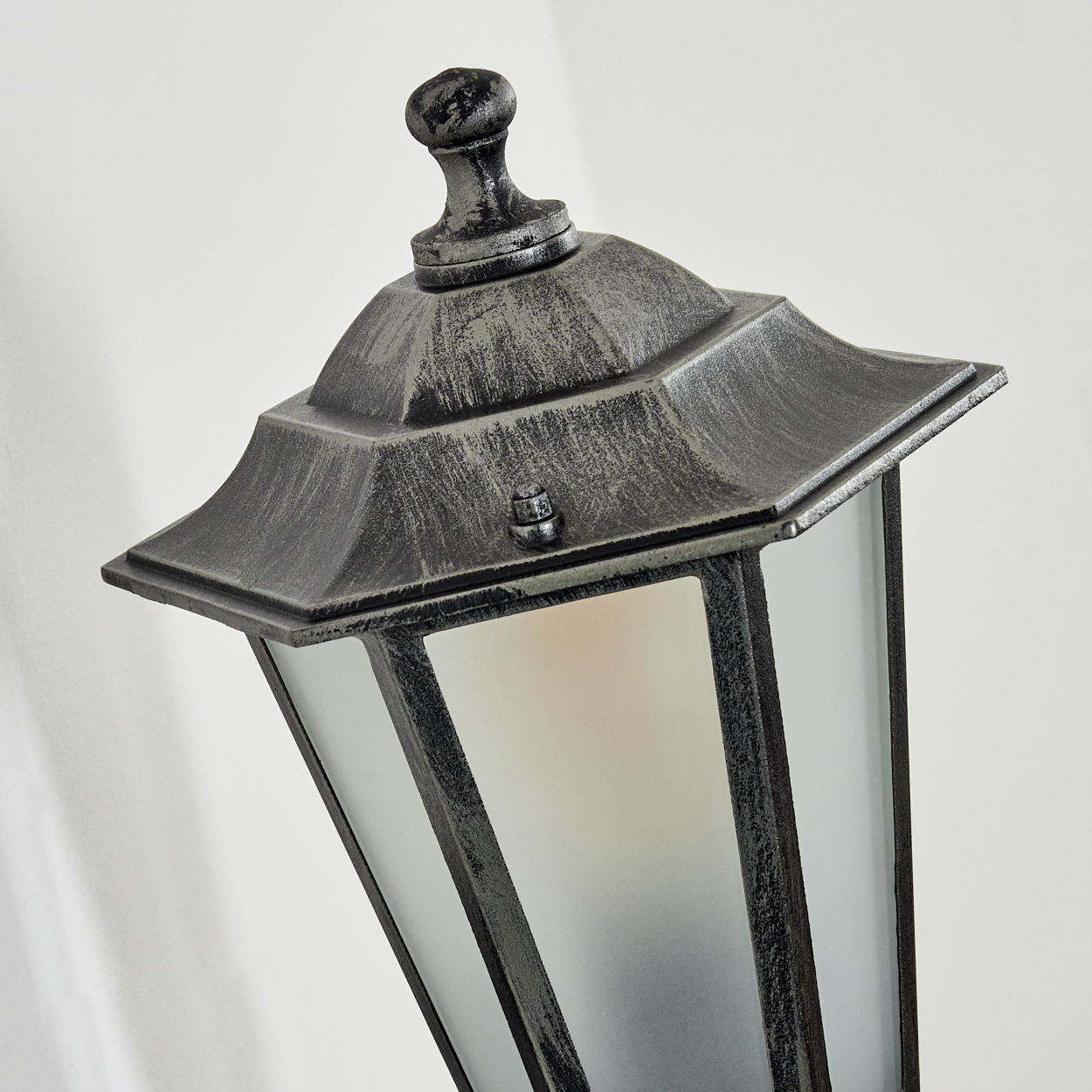 Nahaufnahme einer dekorativen Außenlampe. Sie hat einen Metallrahmen, Milchglasscheiben und eine dekorative Oberseite vor weißem Hintergrund.