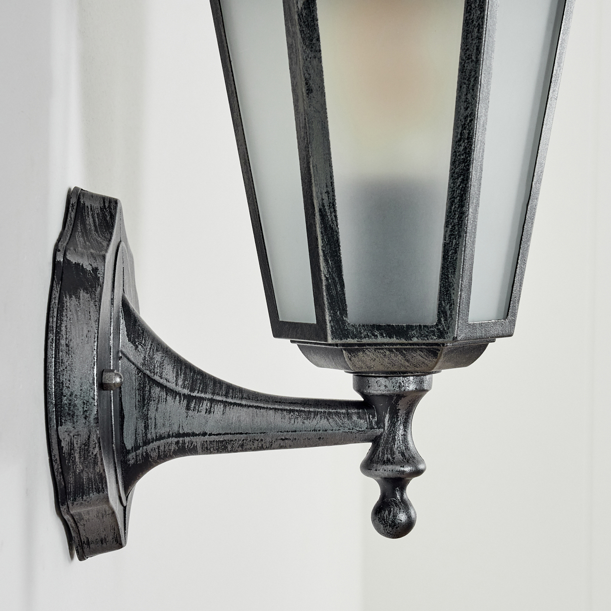 Eine dekorative Wandlampe mit schwarzem Metallrahmen und Milchglasscheiben. Sie ist an einer weißen Wand befestigt.