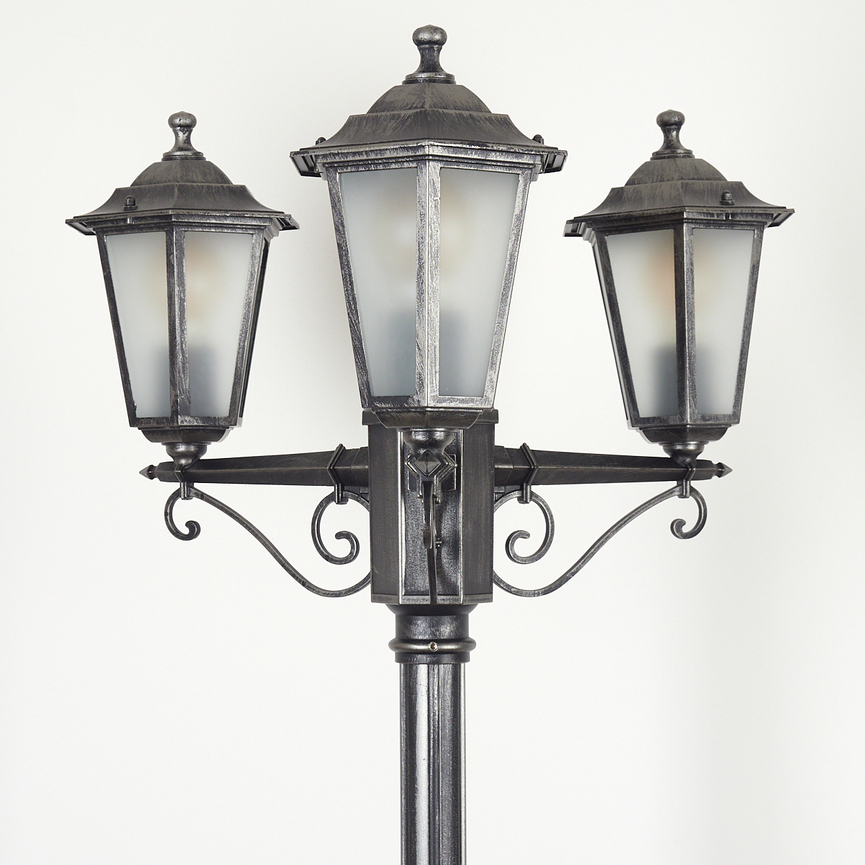 Eine dekorative Straßenlaterne mit drei Köpfen, mattierten Glasscheiben, grau-metallischem Finish und Zierdetails vor weißem Hintergrund.