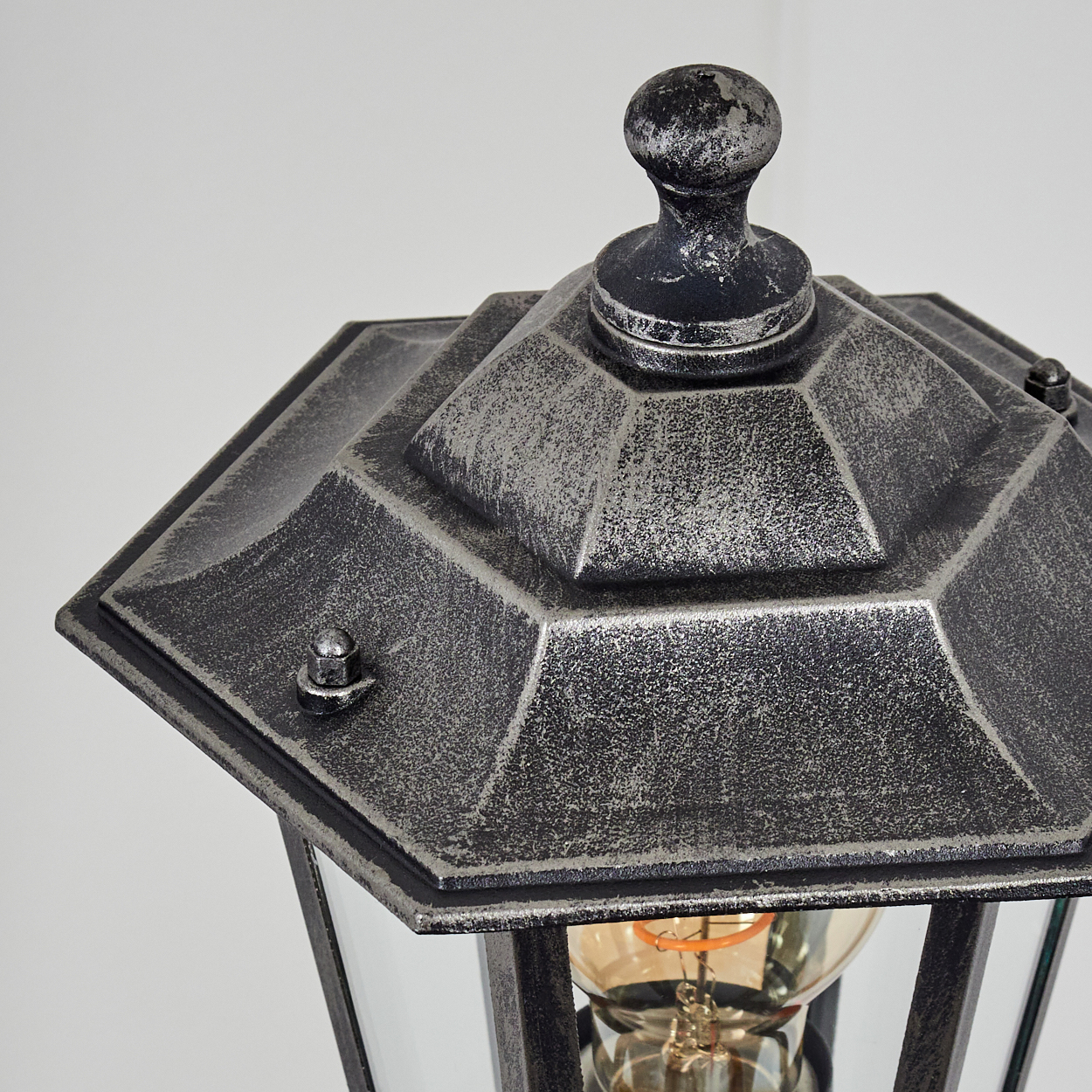 Nahaufnahme einer Vintage-Außenlaterne. Die Laterne ist metallgrau, sechseckig und hat klare Glasscheiben. Der Hintergrund ist weiß.