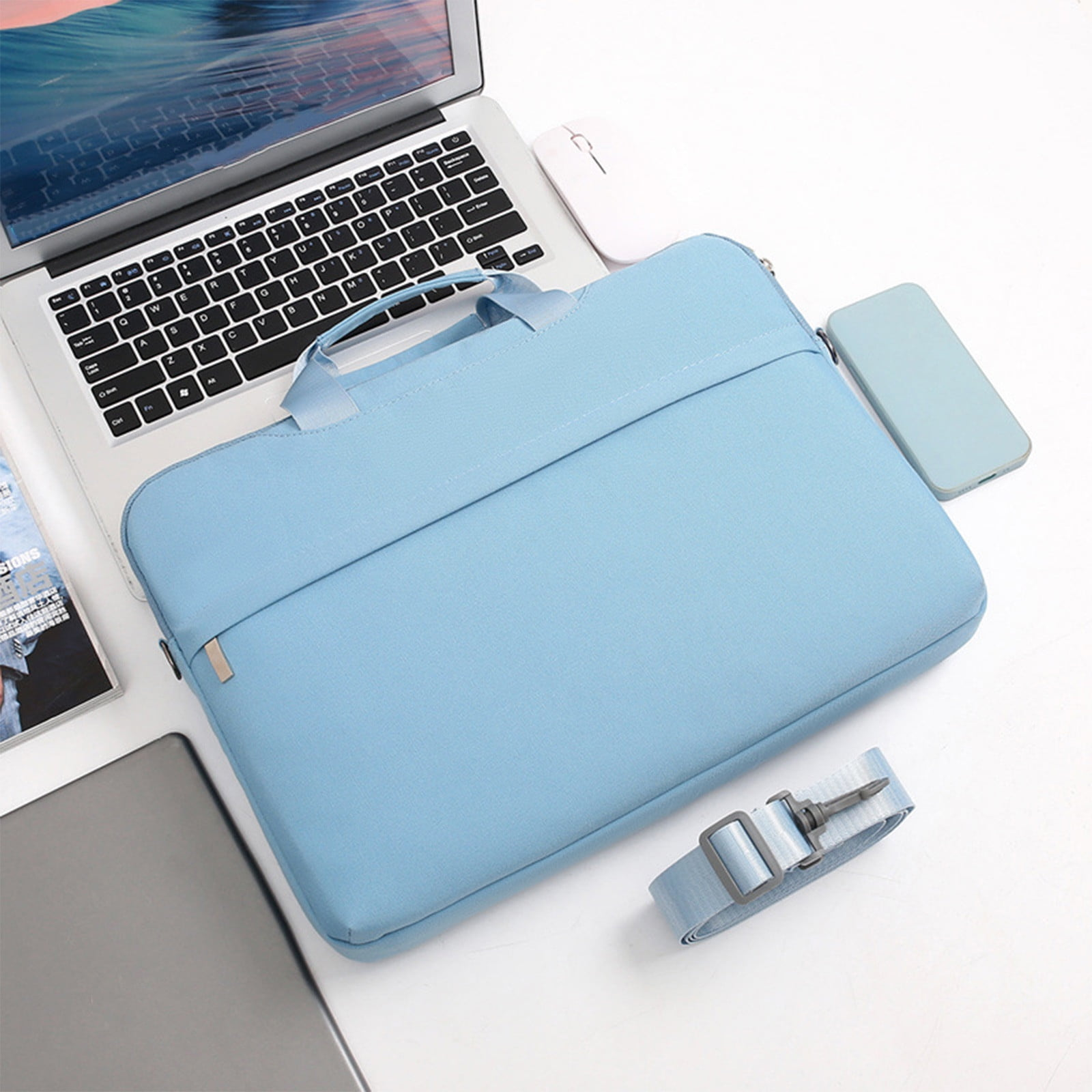 Auf einer weißen Oberfläche befinden sich ein Laptop, eine Maus, ein Telefon und eine hellblaue Laptoptasche. Ein Riemen ist ebenfalls vorhanden.