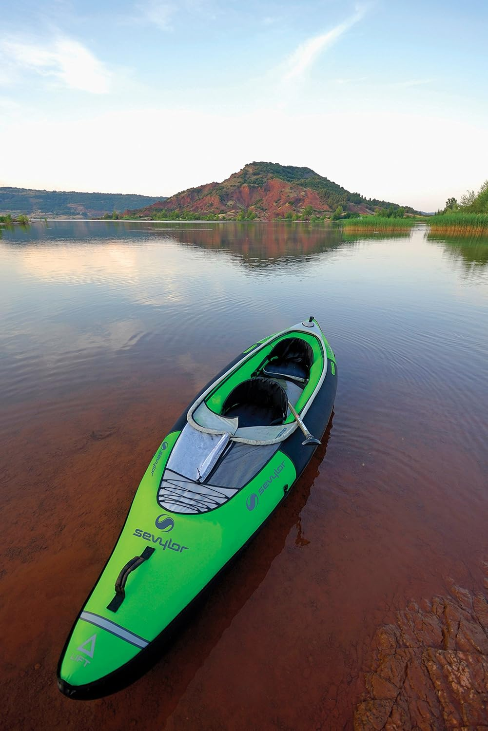Ein grünes Kajak schwimmt auf einem See. Im Hintergrund ist ein Berg zu sehen. Das Wasser ist ruhig und reflektiert den Himmel und den Berg.