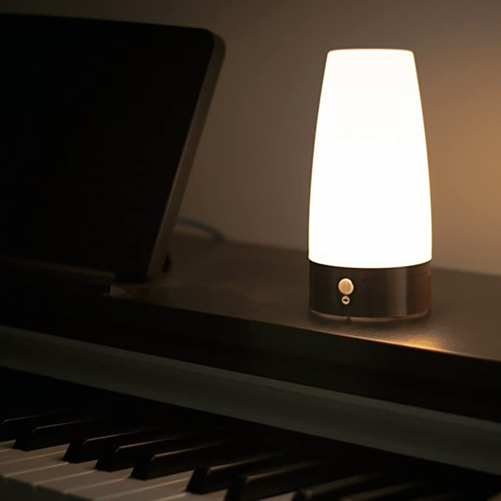 Eine leuchtende Lampe steht auf einem Klavier, die Tastatur ist im Vordergrund sichtbar. Links ist ein Tablet, mit warmem, gedämpftem Licht.