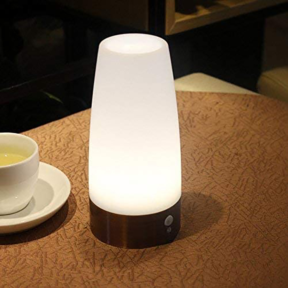 Eine leuchtende weiße und braune Lampe steht auf einem Tisch. Links ist eine Tasse Tee auf einer Untertasse.