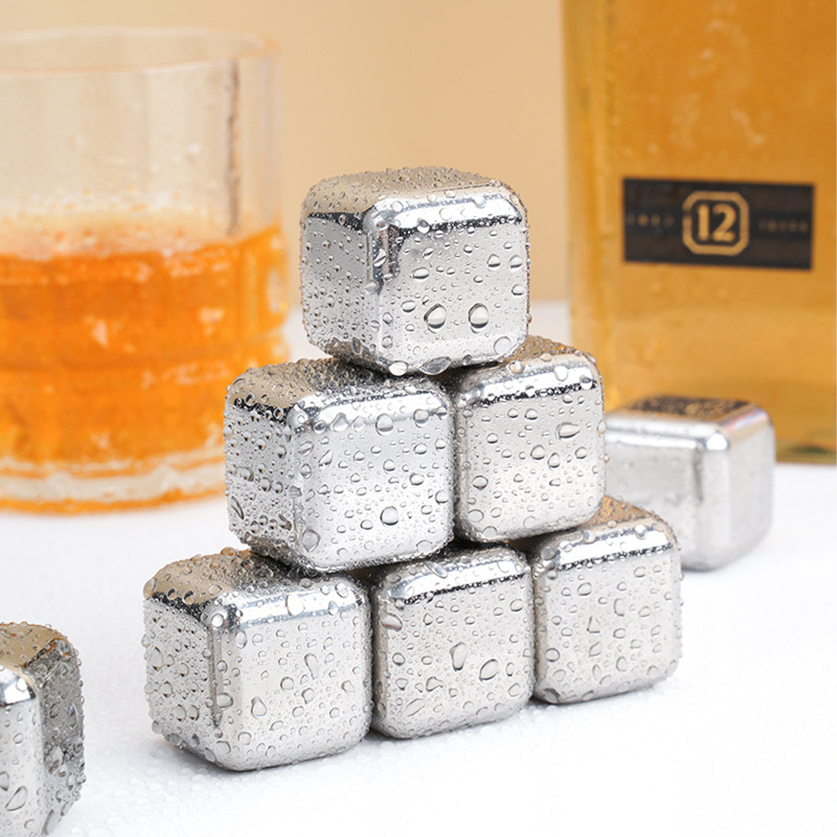 Edelstahl-Eiswürfel, ein Whiskeyglas mit bernsteinfarbener Flüssigkeit und eine Flasche mit 12-Etikett sind sichtbar.