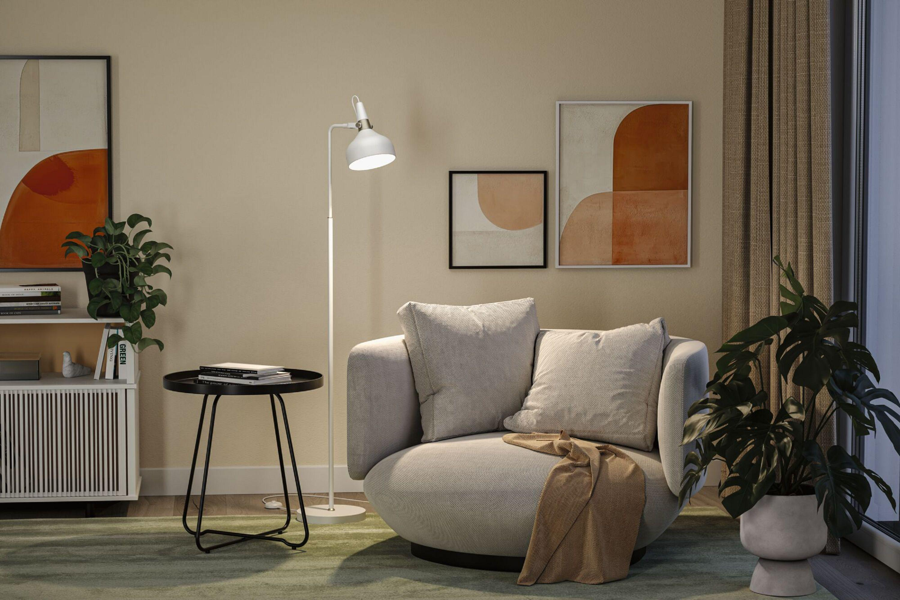 Ein modernes Wohnzimmer mit grauem Sofa, Stehlampe und Kunstwerken. Pflanzen und ein Beistelltisch ergänzen die Szene.