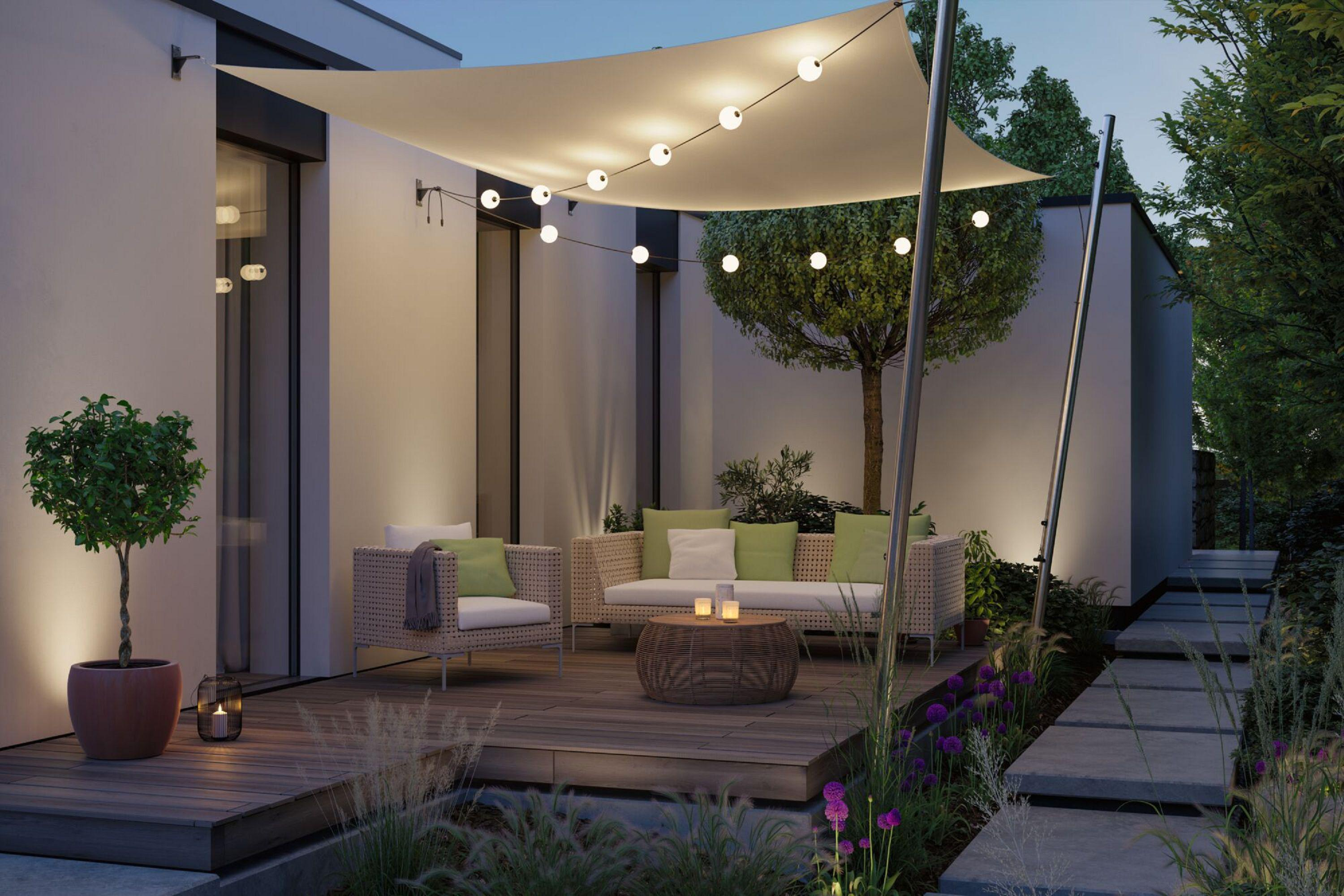 Patio na zewnątrz z miejscami do siedzenia, girlandami świetlnymi i roślinami. Scena wieczorna z oświetloną atmosferą. Przytulna, zachęcająca przestrzeń.