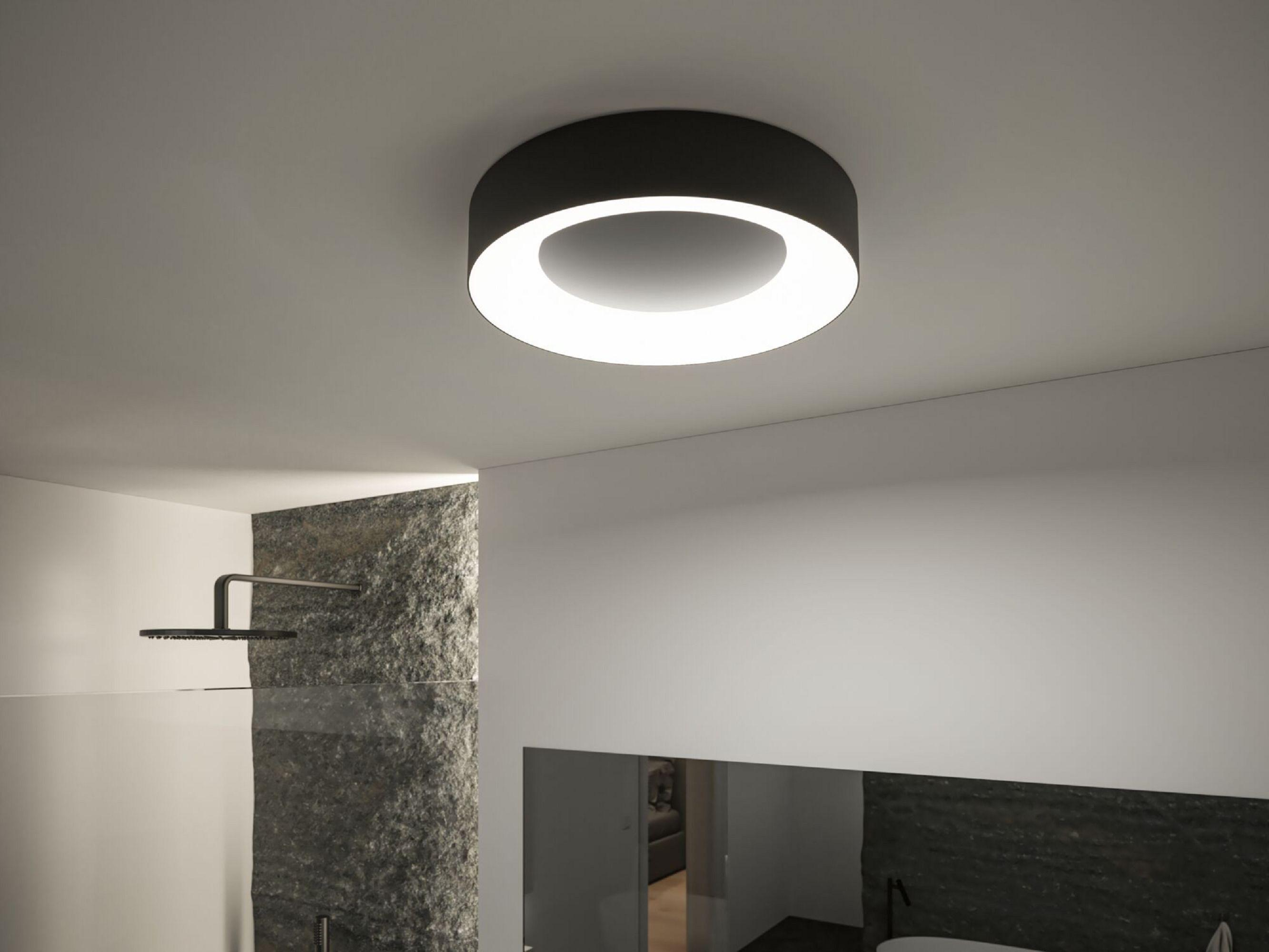Nowoczesna łazienka z okrągłą lampą. Widoczna kamienna ściana i głowica prysznicowa.