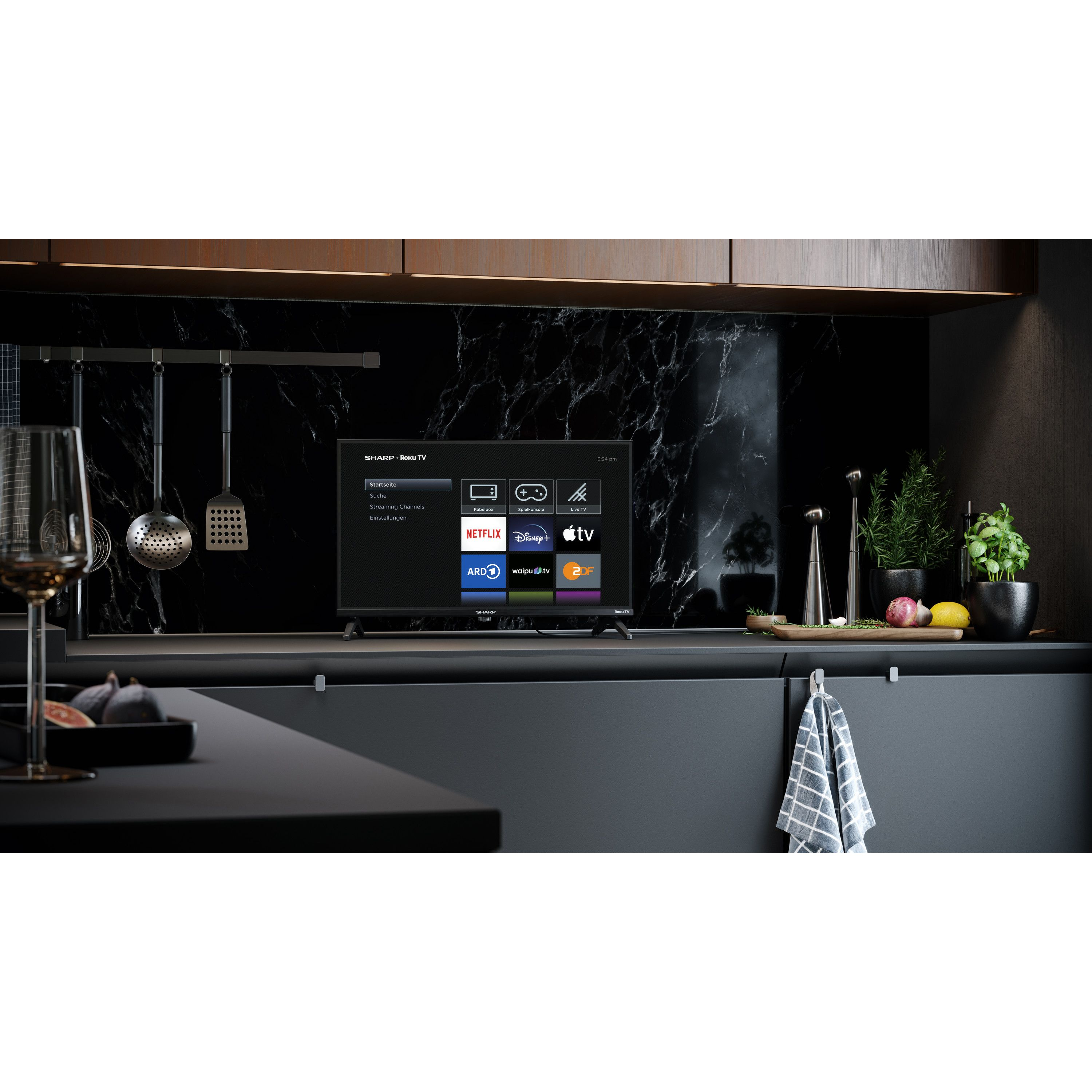 Küchenszene mit Fernseher, Obst und Kräutern. Im Vordergrund steht ein Glas. Hintergrund hat Marmor und Schränke.