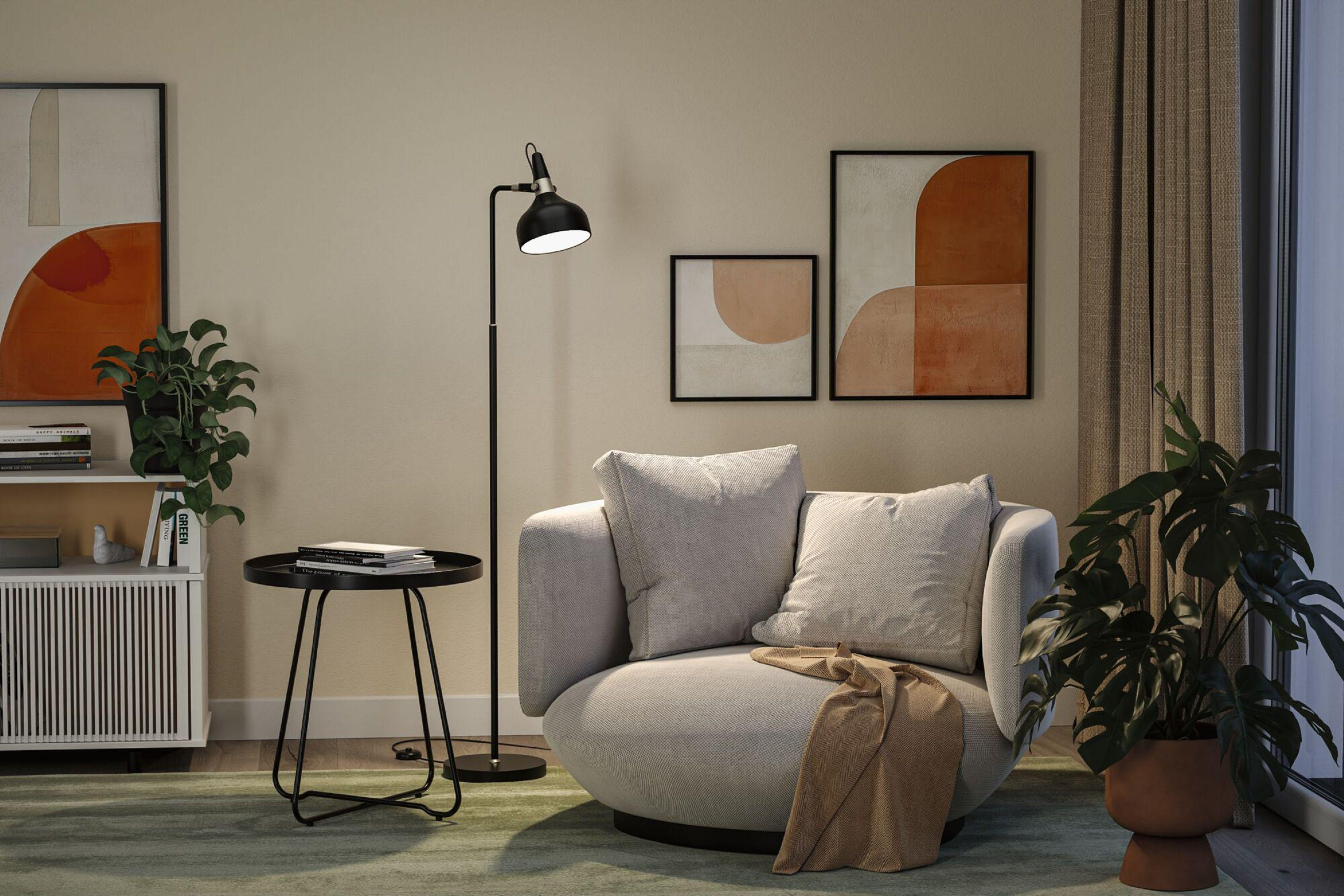 Modernes Wohnzimmer mit grauem Sofa, schwarzer Lampe, Kunstwerken, Pflanzen und einem kleinen Tisch auf grünem Teppich.