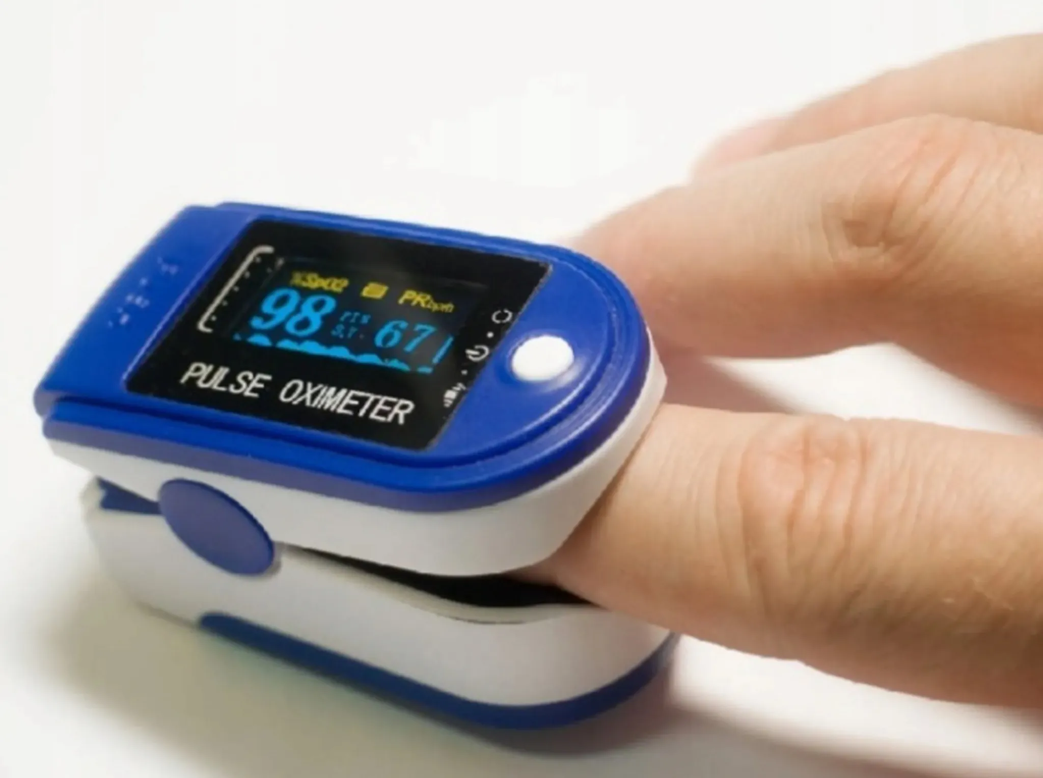 Ein Pulsoximeter am Finger zeigt SpO2 98% und PR 67 bpm an. Das Gerät ist blau und weiß, mit dem Finger eingesetzt.