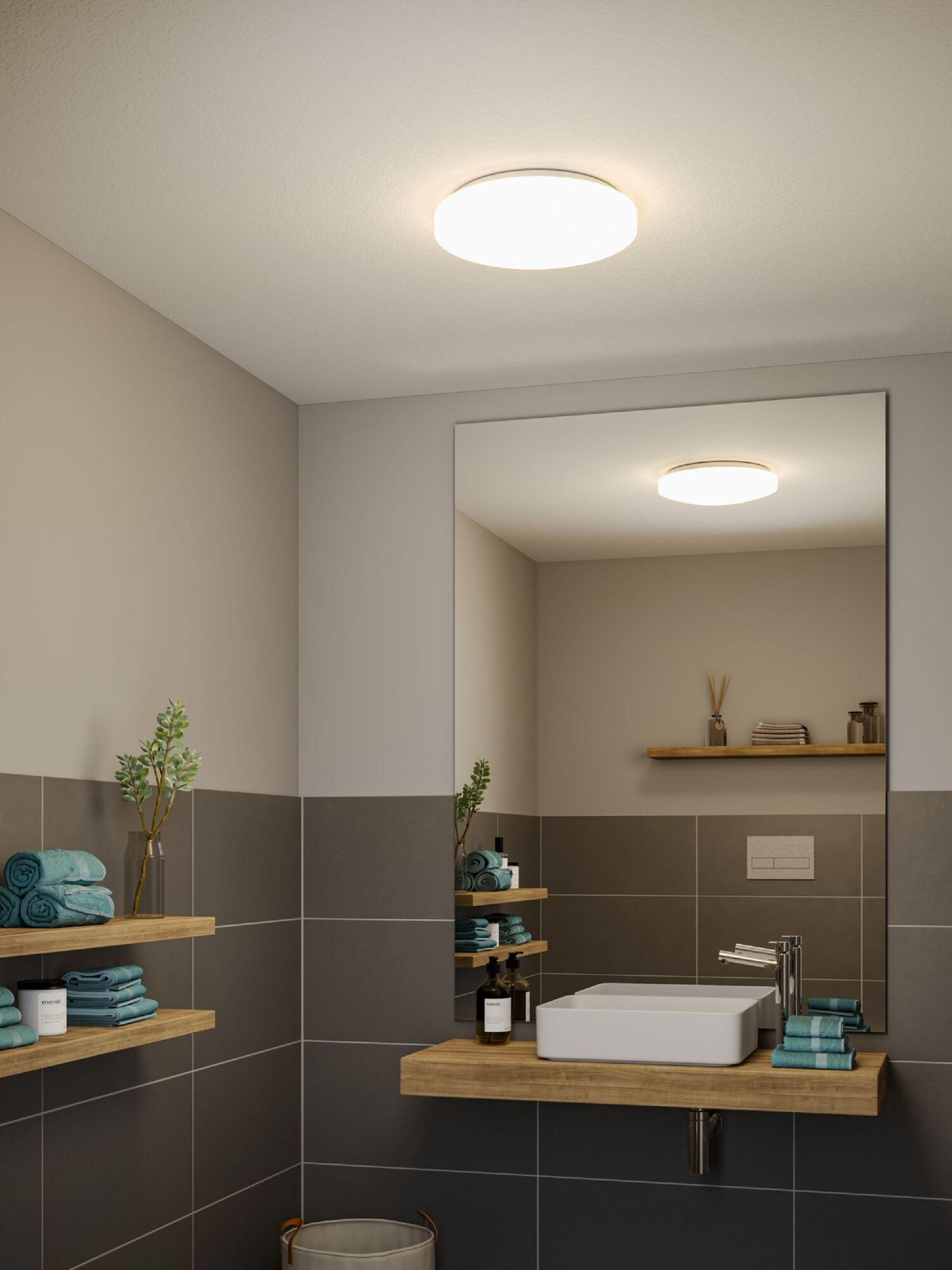 Scène de salle de bain avec un grand miroir, un lavabo, des étagères avec des serviettes et un plafonnier. Tons gris et marron.