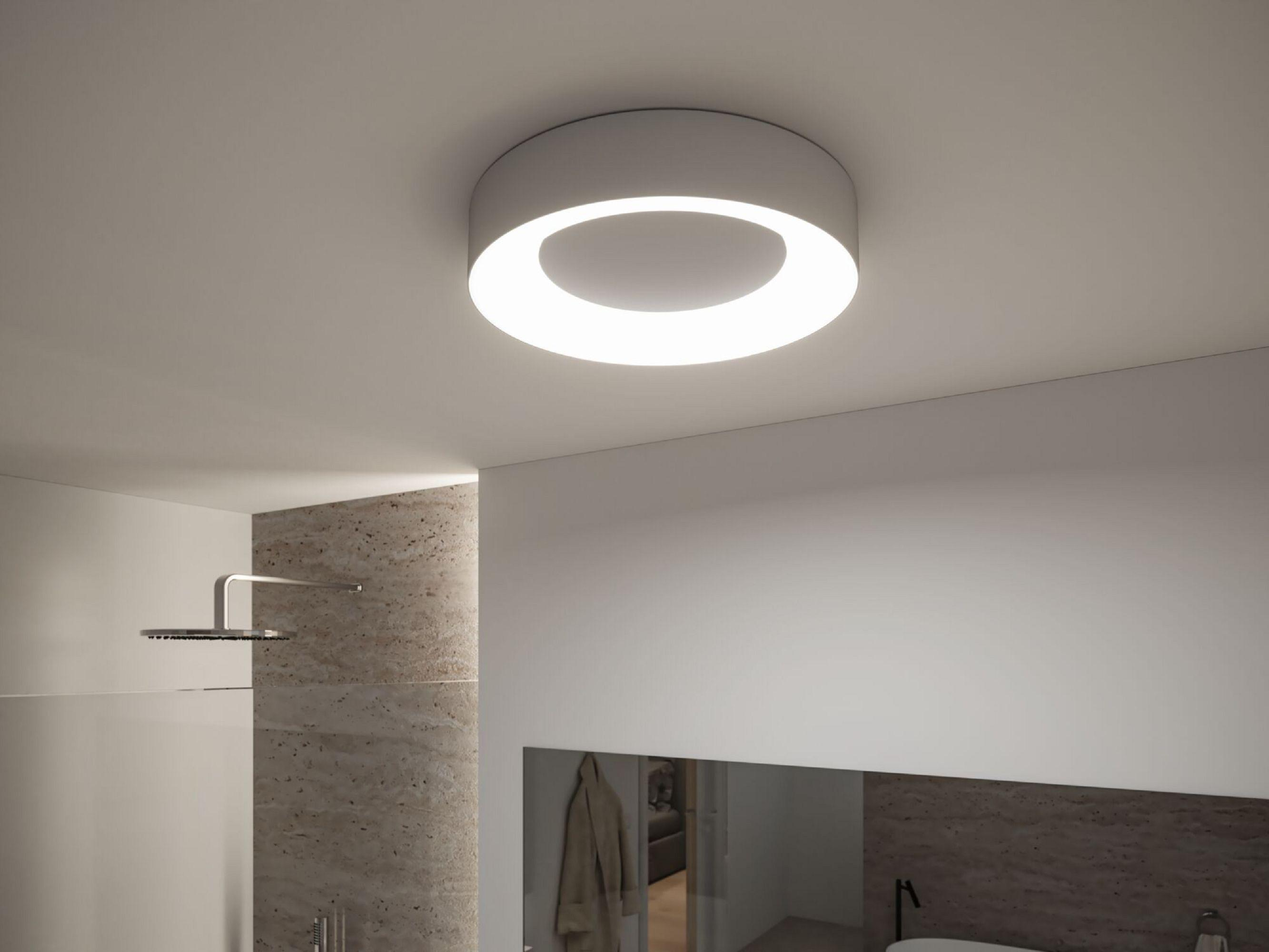 Une salle de bain moderne avec un plafonnier circulaire. Une douche et un miroir sont visibles.