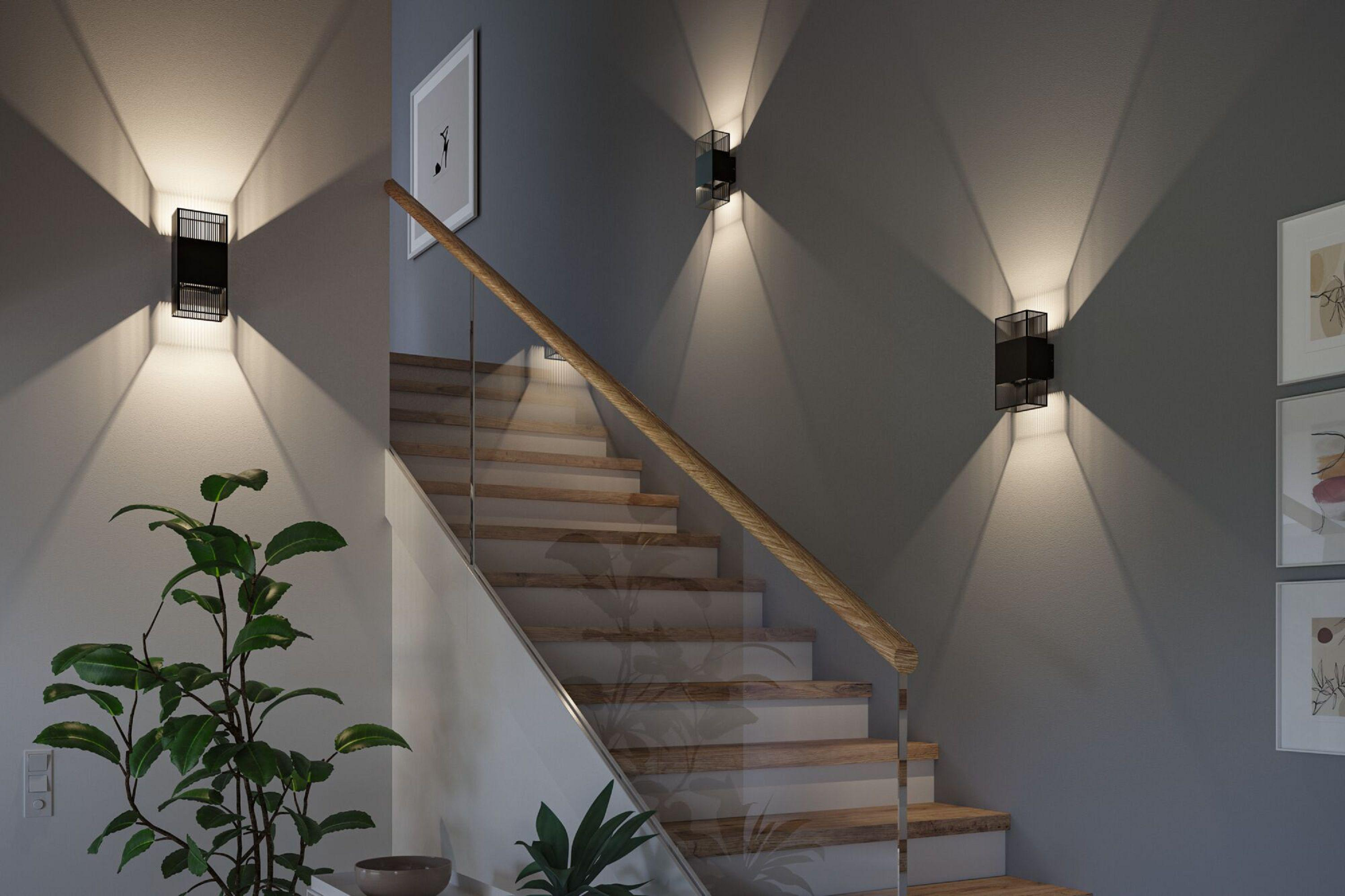 Un escalier moderne avec des marches en bois, une balustrade en verre et des appliques murales noires. Une plante en avant-plan.