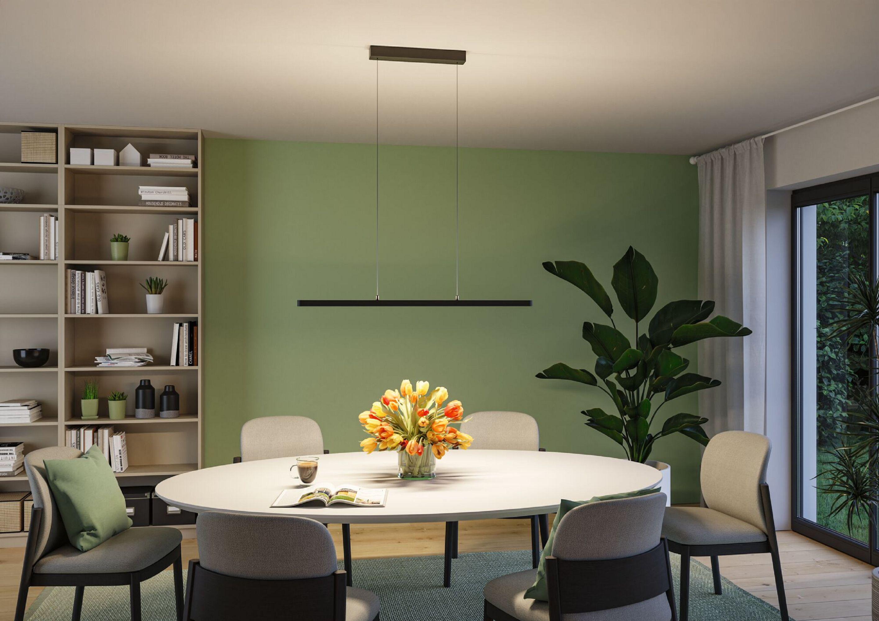Jadalnia z owalnym stołem, kwiatami, krzesłami i zieloną ścianą. Regał po lewej, roślina po prawej i okno.
