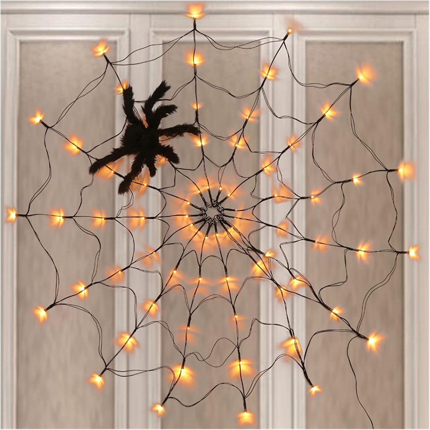 Eine dekorative Halloween-Spinne mit Lichtern und einer schwarzen Spinnendekoration vor einem weißen Türhintergrund.