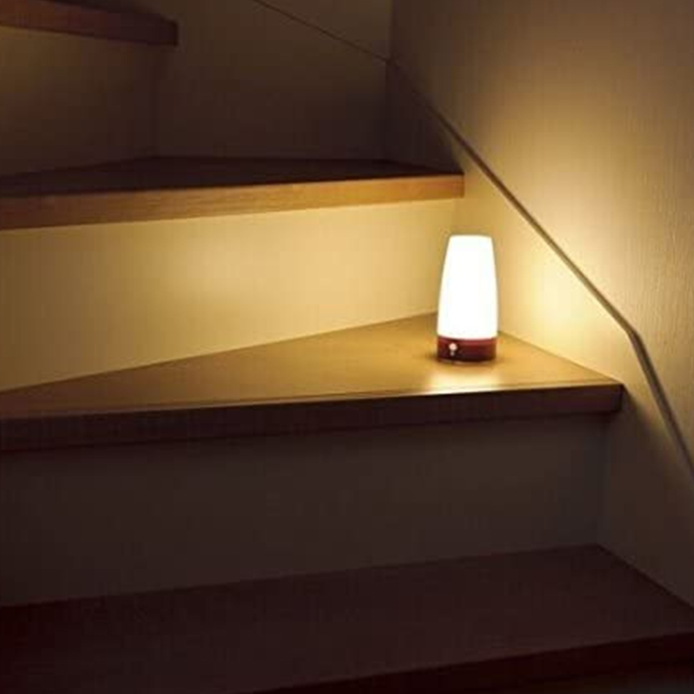 Eine beleuchtete Lampe steht auf einem Treppenabsatz aus Holz. Die Lampe ist weiß und rot. Die Treppe und die Wand sind hellbraun.