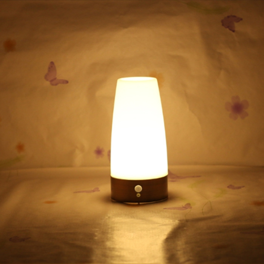 Eine leuchtende Lampe mit Holzsockel steht auf einer Oberfläche. Der Hintergrund zeigt Schmetterlinge und Blumen auf strukturiertem Papier.