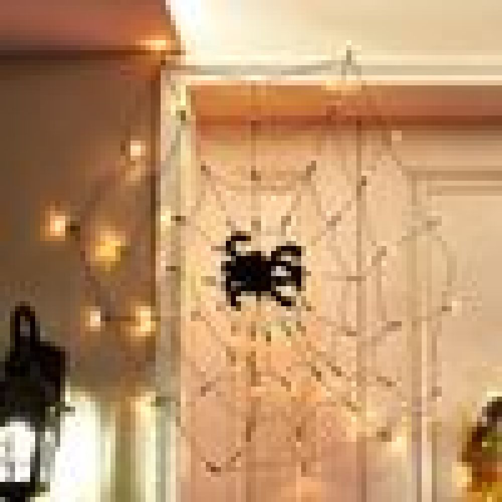 Eine Halloween-Dekoration mit einem Spinnennetz und einer großen schwarzen Spinne. Warme Lichter schmücken das Netz. Der Hintergrund ist eine Wand und Decke.