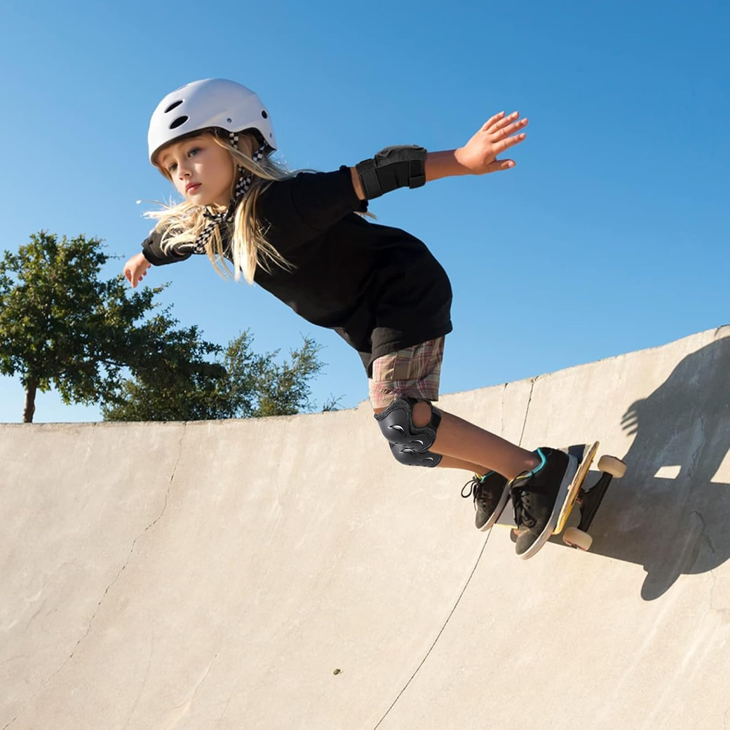 Ein Mädchen auf einem Skateboard in einem Skatepark, mit Helm und Protektoren. Sie ist in der Luft vor blauem Himmel und führt einen Trick aus.