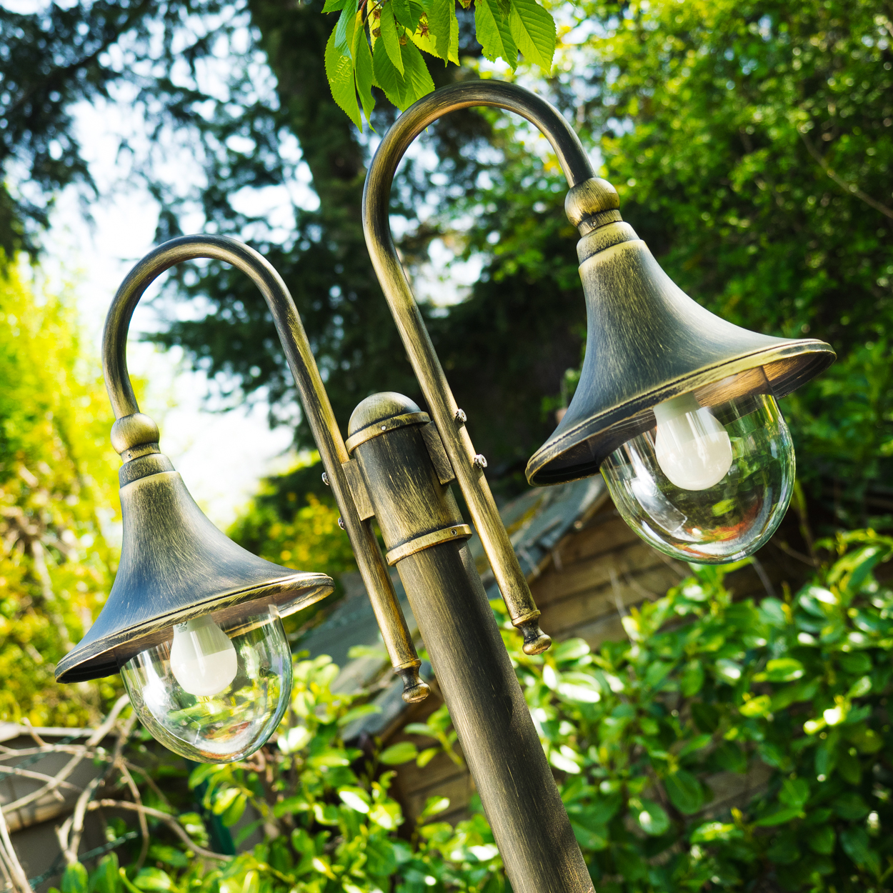 Zwei antike Gartenlampen mit Glaskugeln und dunklem Metallfinish, umgeben von grünem Laub.