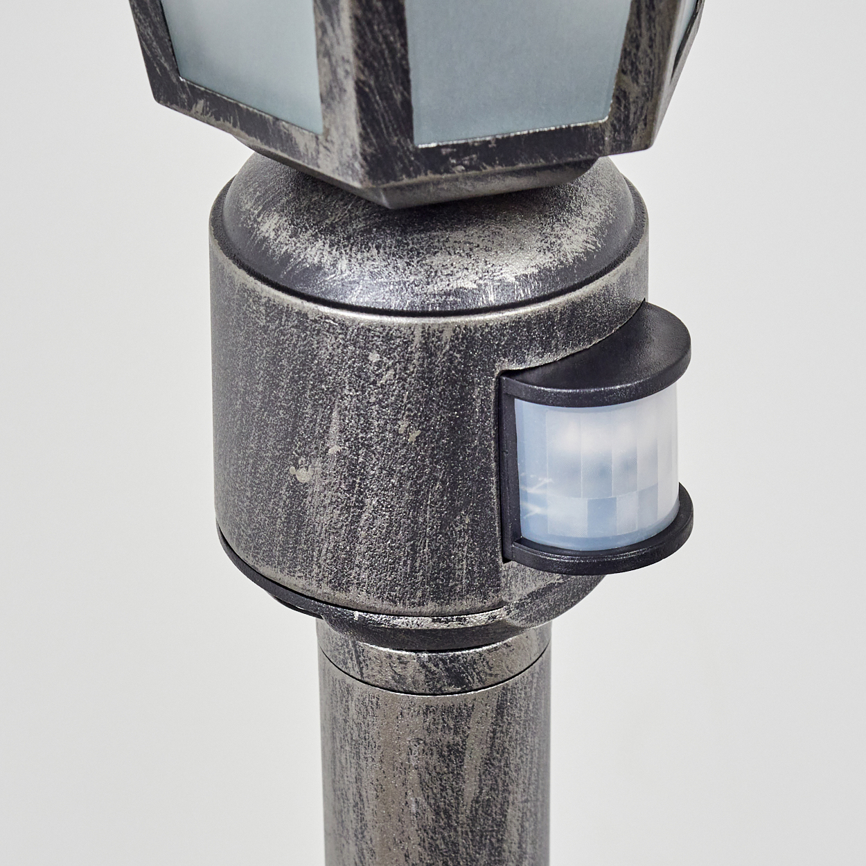 Nahaufnahme einer metallischen Außenlaterne mit Sensor. Die Lampe hat einen Glaskopf und einen Sensor an der Seite.