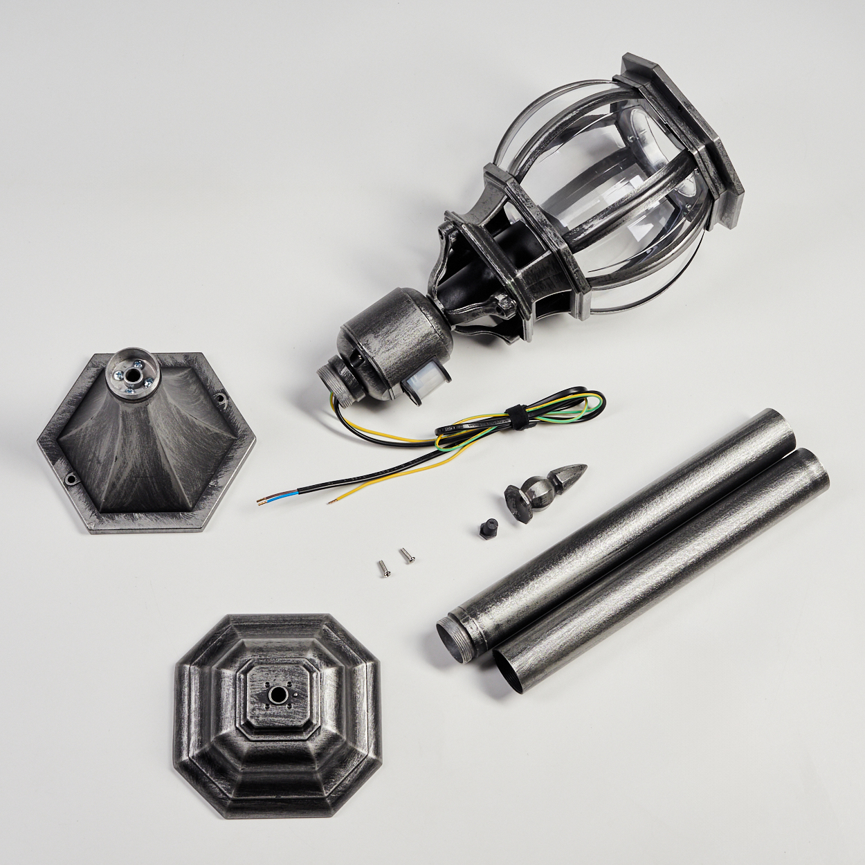 Zerlegte Außenlampe auf weißem Hintergrund. Enthält Lampenkopf, Pfosten, Sockel und elektrische Komponenten. Metallische Farbe und klares Glas.