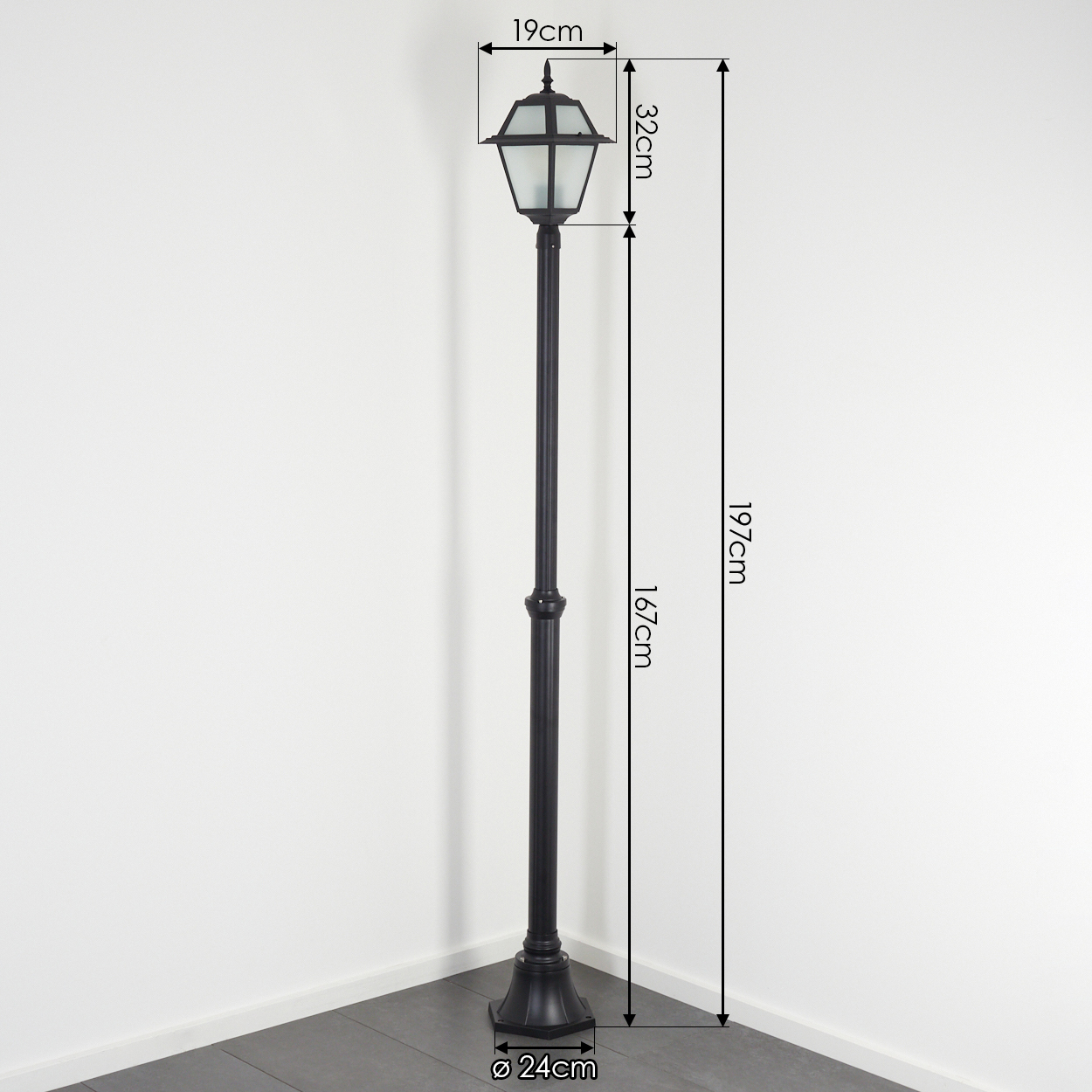 Eine schwarze Außenlaterne mit sechseckigem Oberteil und Sockel. Die Abmessungen sind angegeben. Sie steht in einer Ecke.