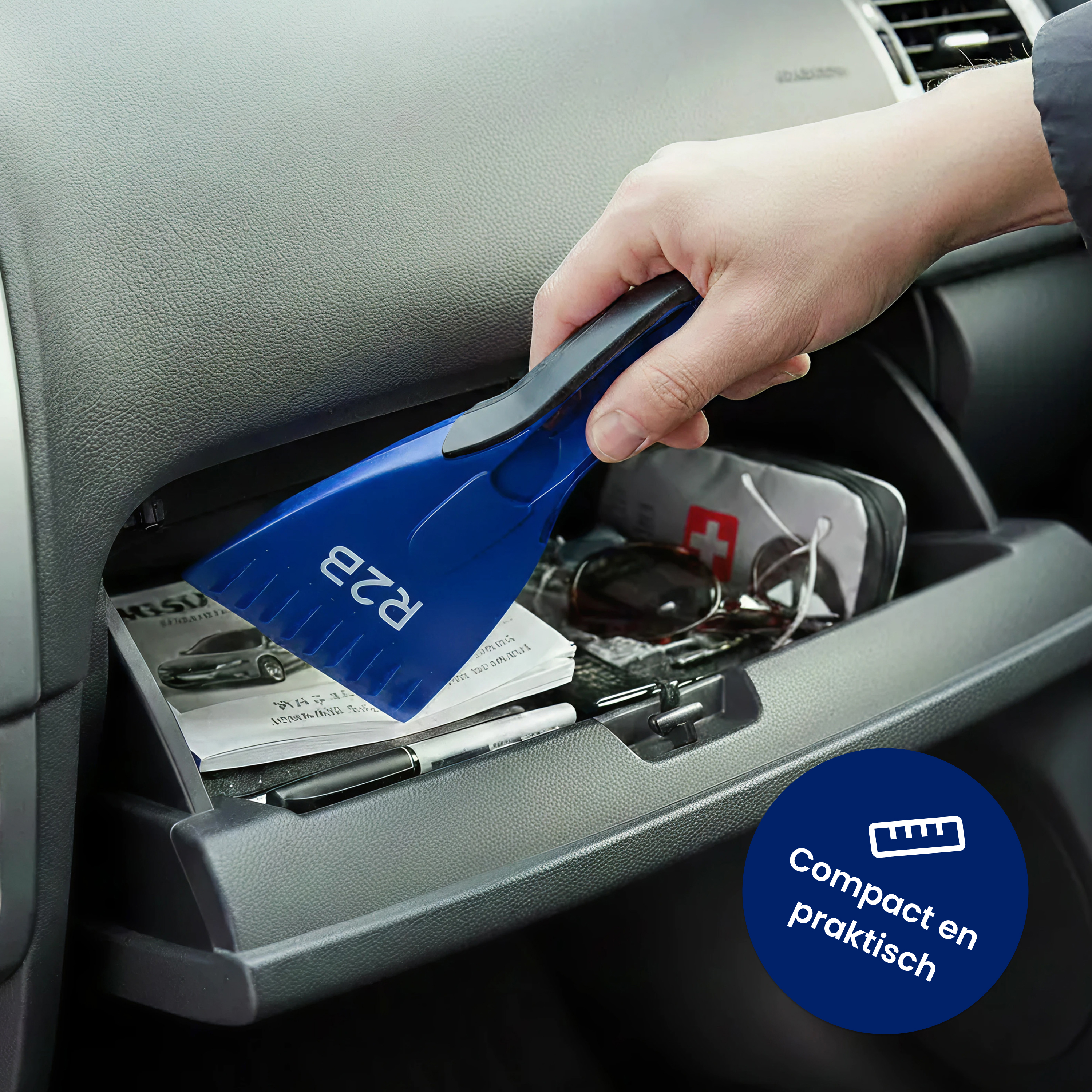 Eine Hand legt einen blauen Eiskratzer in das Handschuhfach eines Autos. Das Fach enthält Stifte, Sonnenbrillen.