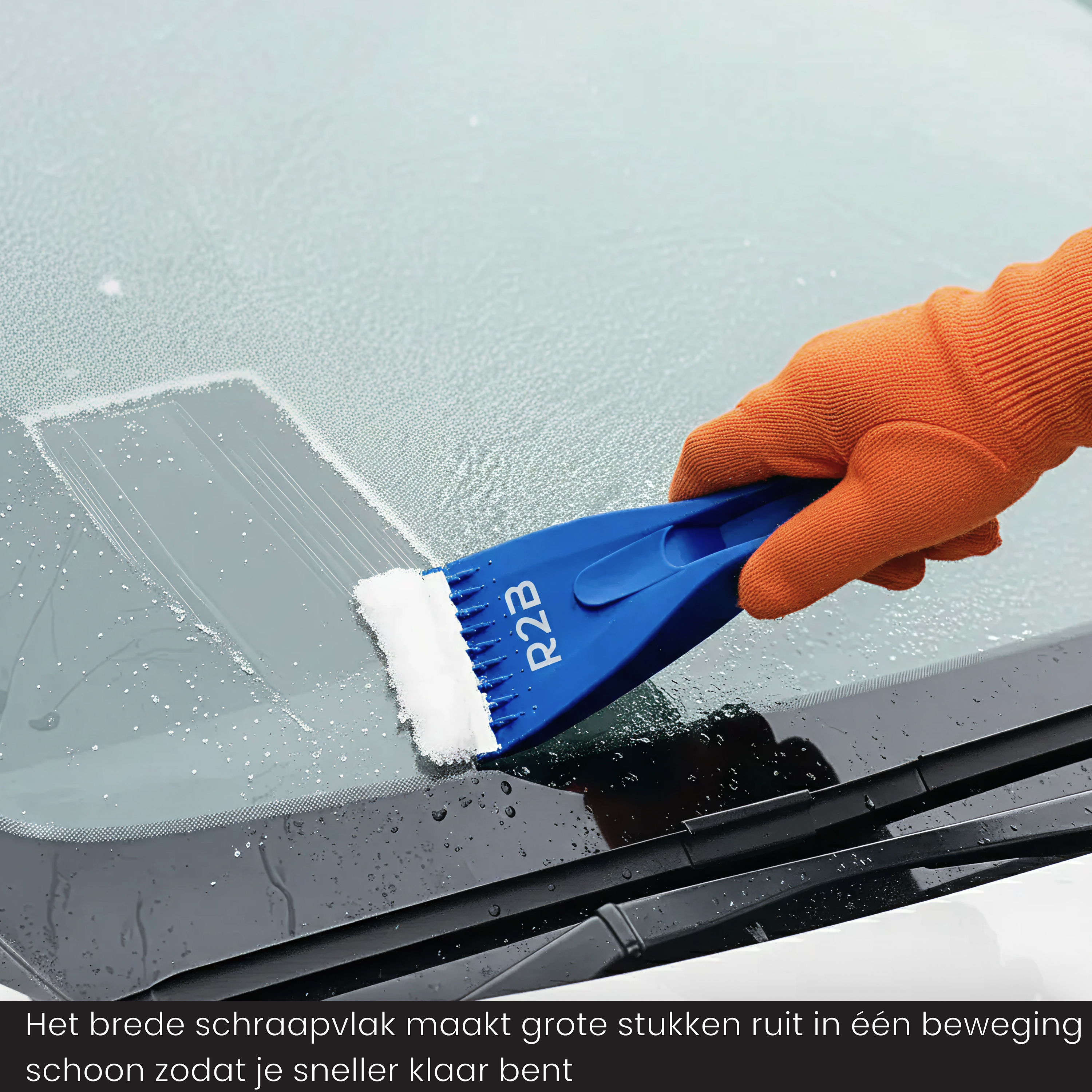 Eine Hand mit einem orangefarbenen Handschuh hält einen blauen Eisschaber und reinigt eine gefrorene Windschutzscheibe.