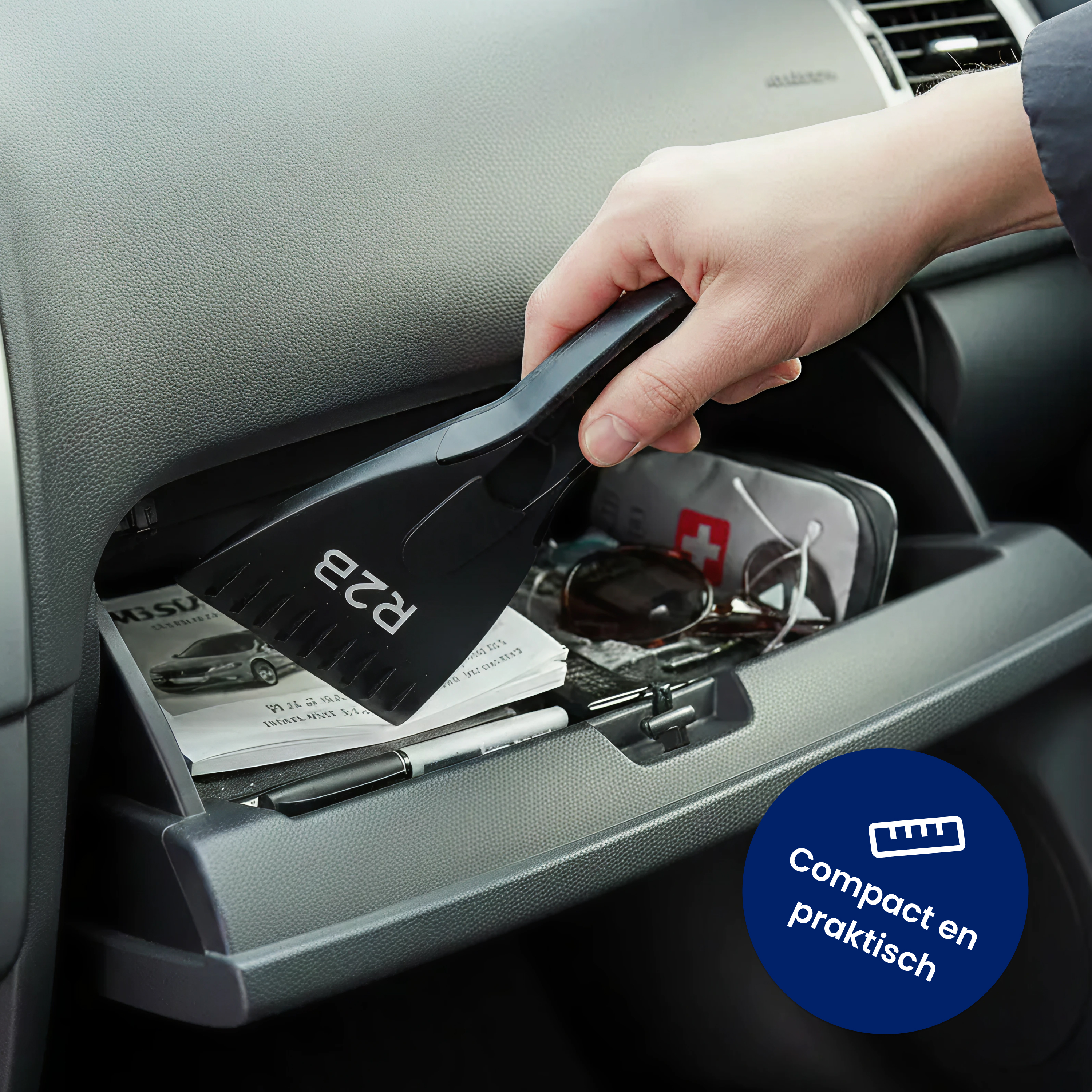 A hand places a black ice scraper into a car's glove compartment, which also holds documents and accessories.