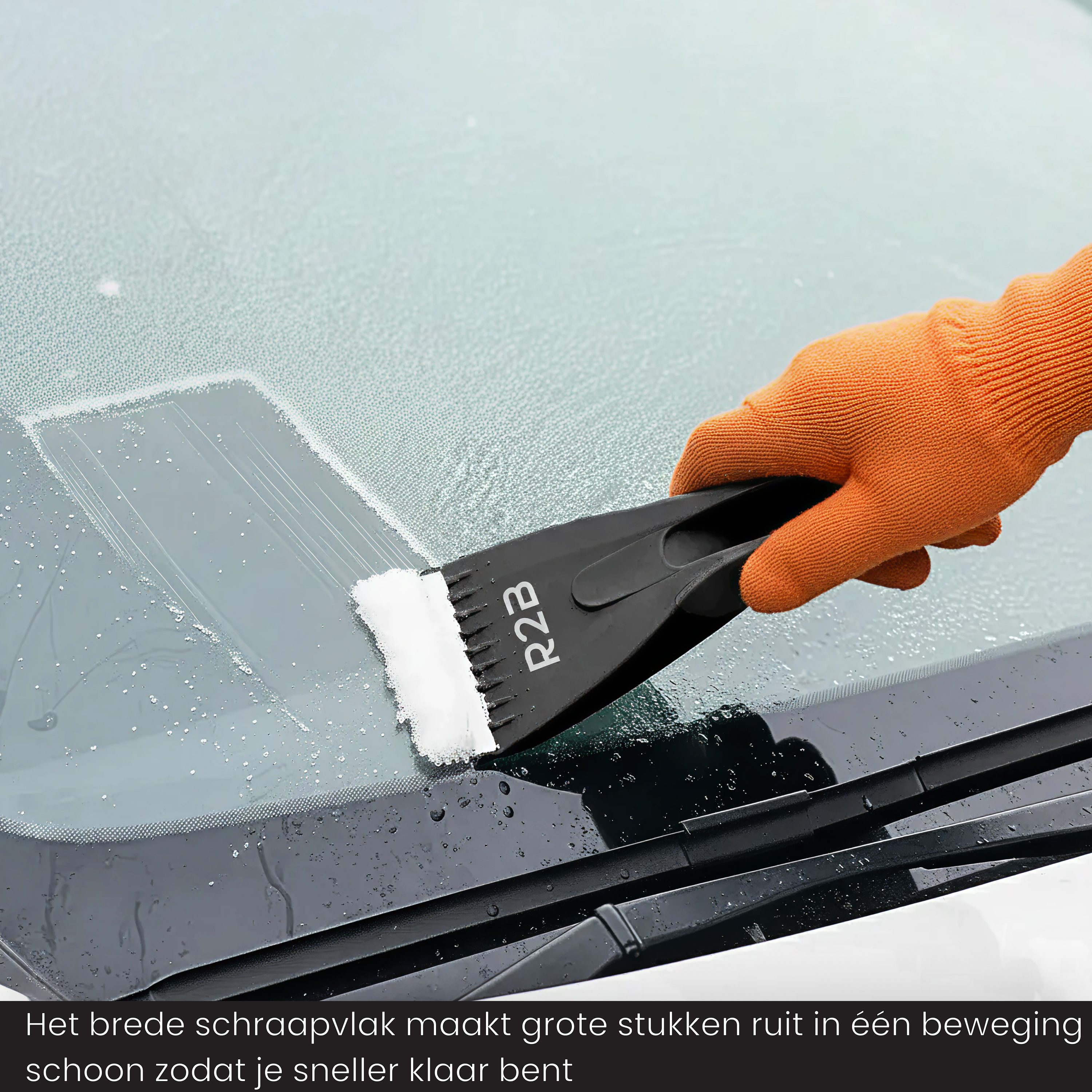 A hand wearing an orange glove scrapes ice from a windshield with a black ice scraper.