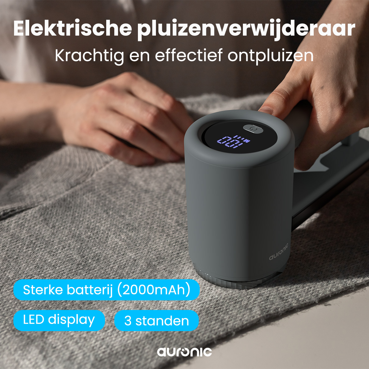 Un rasoir à peluches électrique gris est tenu au-dessus d'un pull gris. Il a un affichage numérique et le texte indique 'Sterke batterij (2000mAh)'.