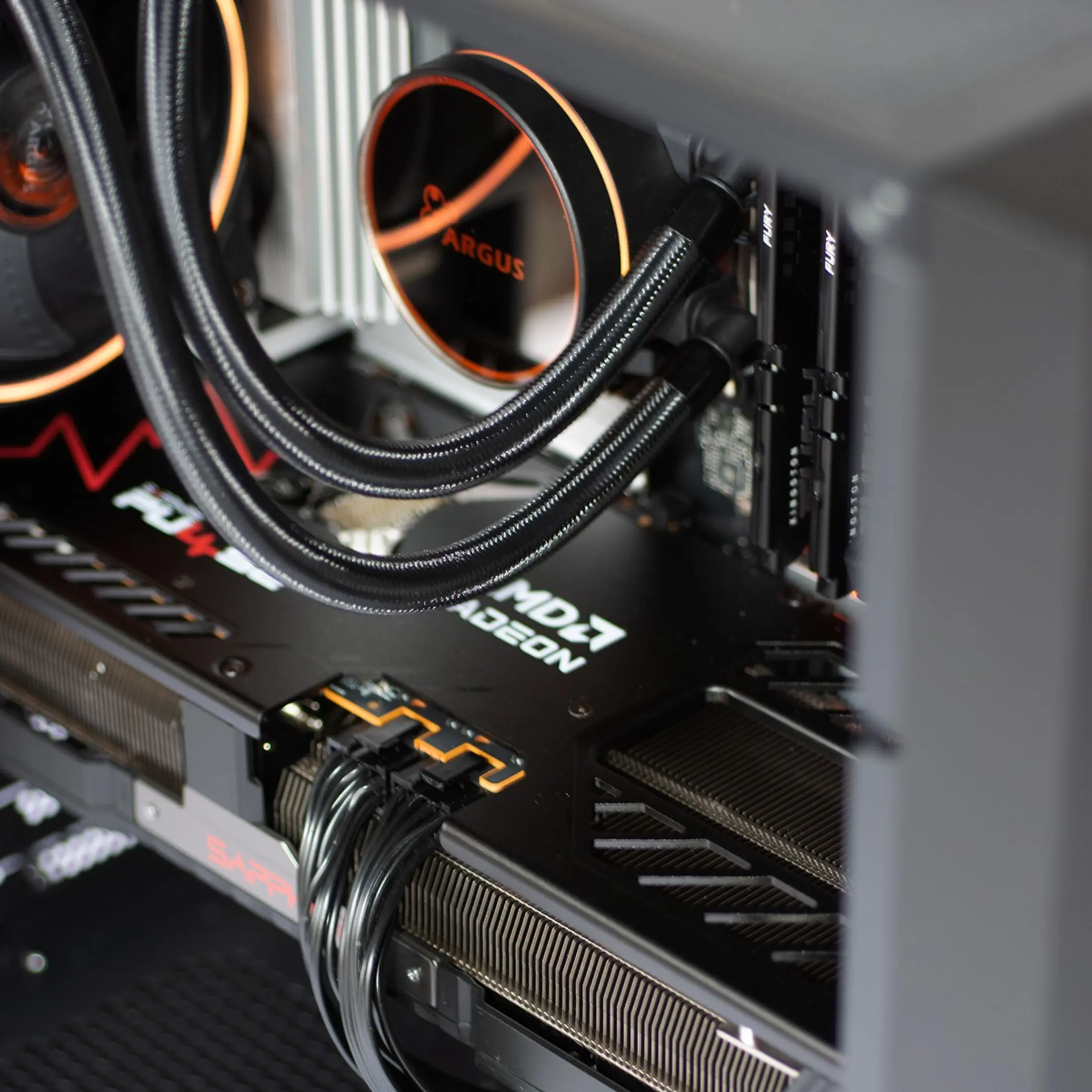 Close-up van een pc-component. Vloeistofkoeler met oranje licht, zwarte buizen en grafische kaart met 'AMD Radeon'.