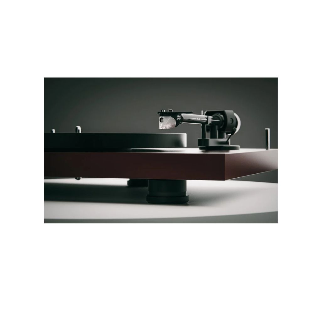 Zbliżenie gramofonu. Ma czarne ramię z wkładką, brązową podstawę i czarne podpory na białej powierzchni.