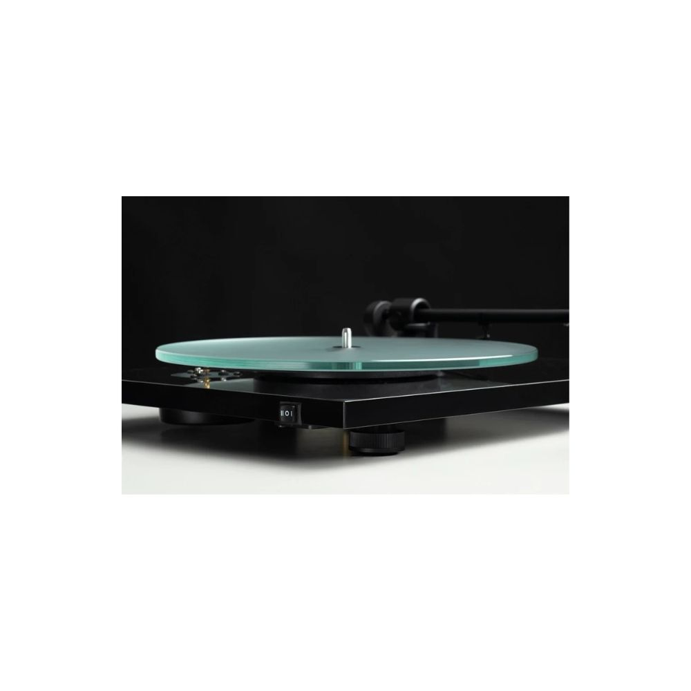 Czarny gramofon z zielonym szklanym talerzem stoi na białej powierzchni na czarnym tle. Widoczny jest włącznik zasilania.