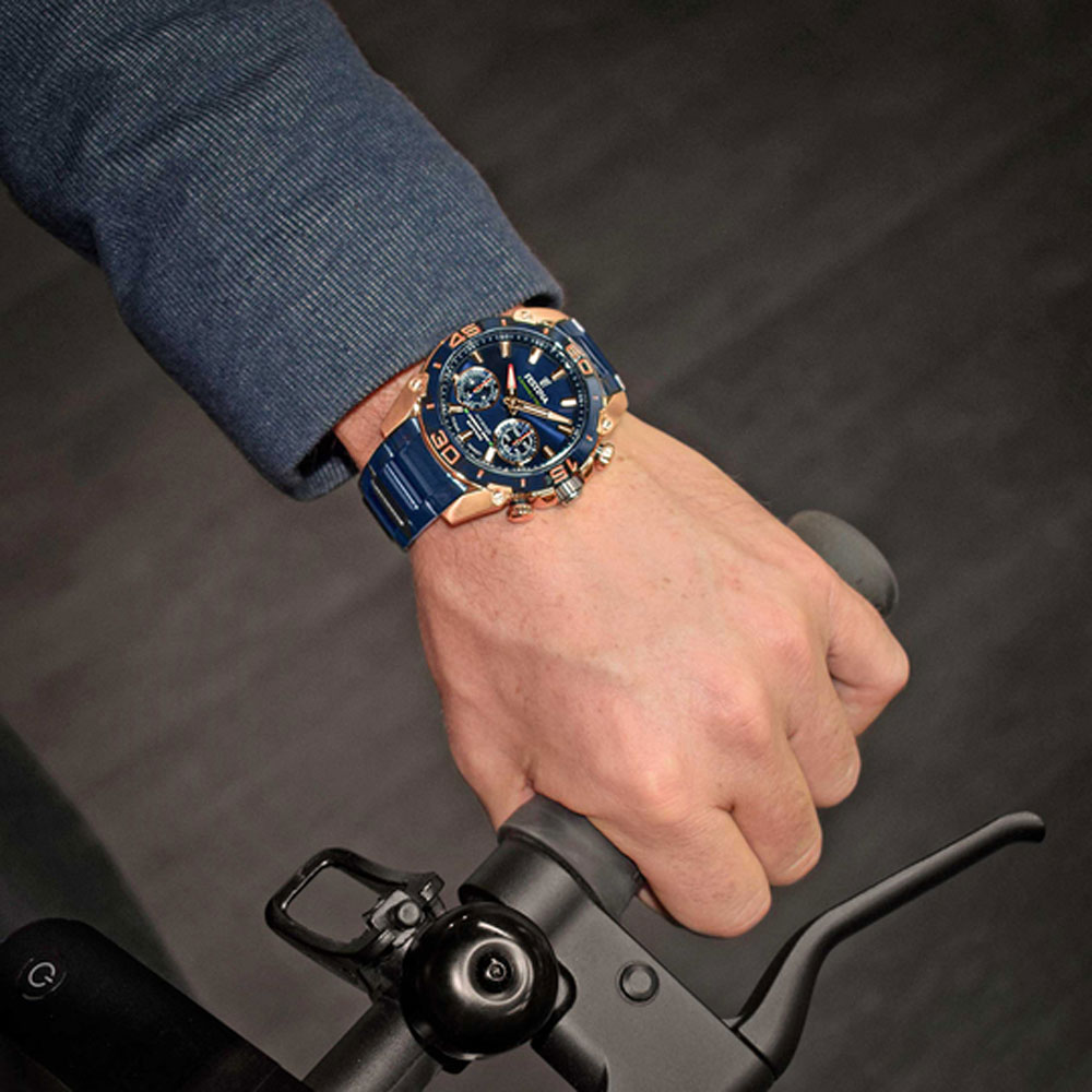 Eine Hand mit einer blau-goldenen Uhr hält einen Fahrradlenker. Der Hintergrund ist verschwommen.