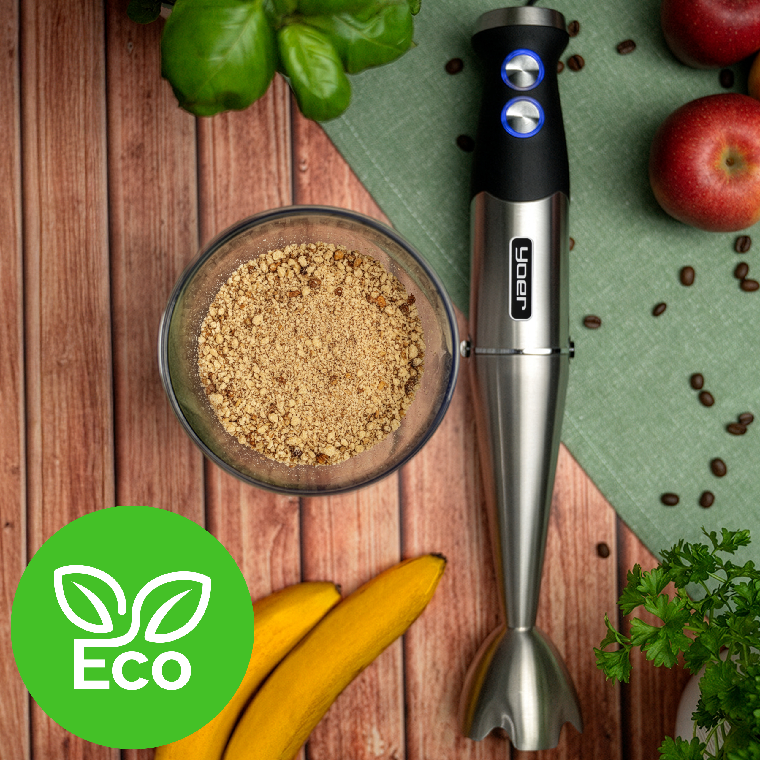 Blender, miska orzechów, banany, jabłka i zioła na drewnianej powierzchni. Widoczne logo 'Eco'.