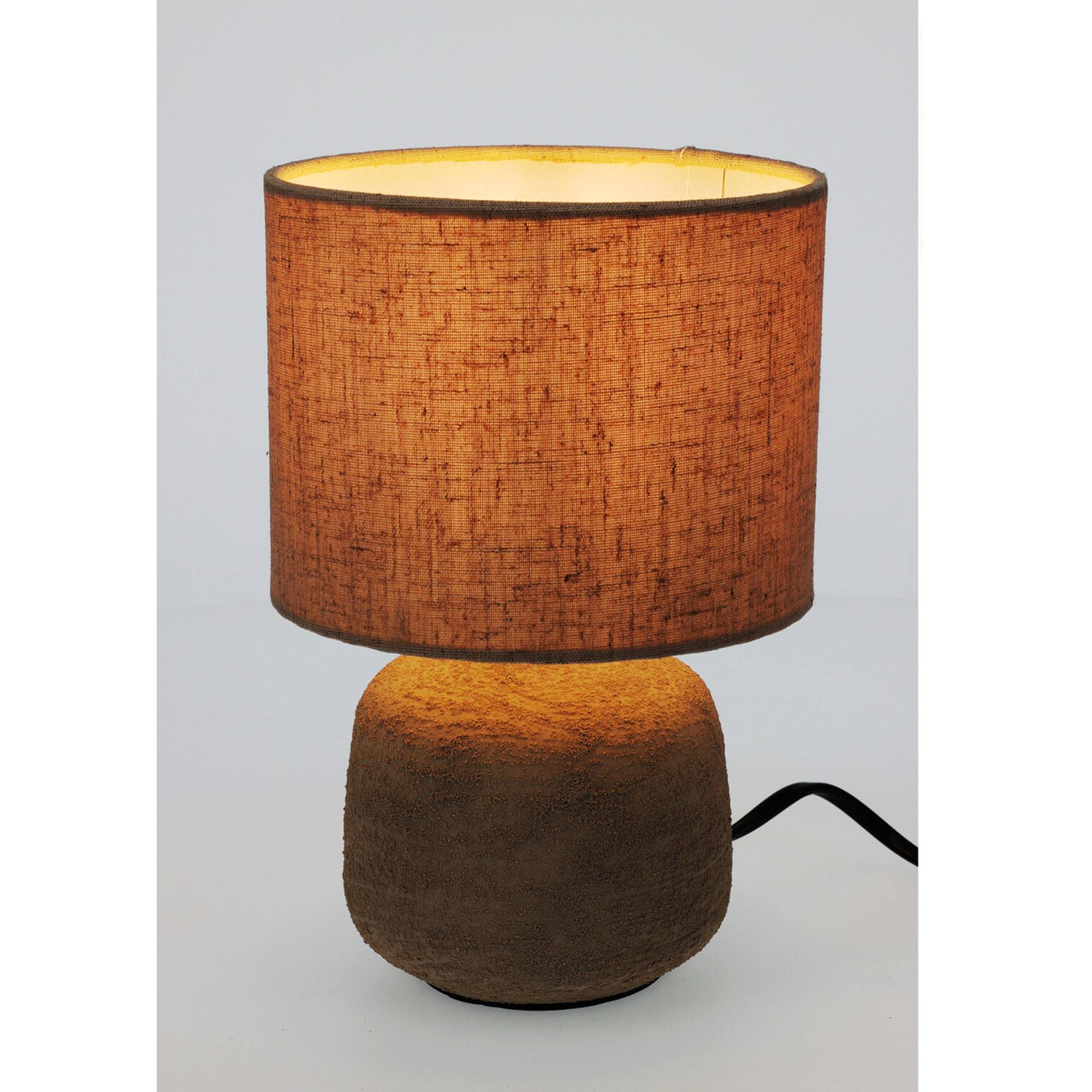Una lámpara de mesa con base y pantalla marrón texturizada. La pantalla es cilíndrica e iluminada.