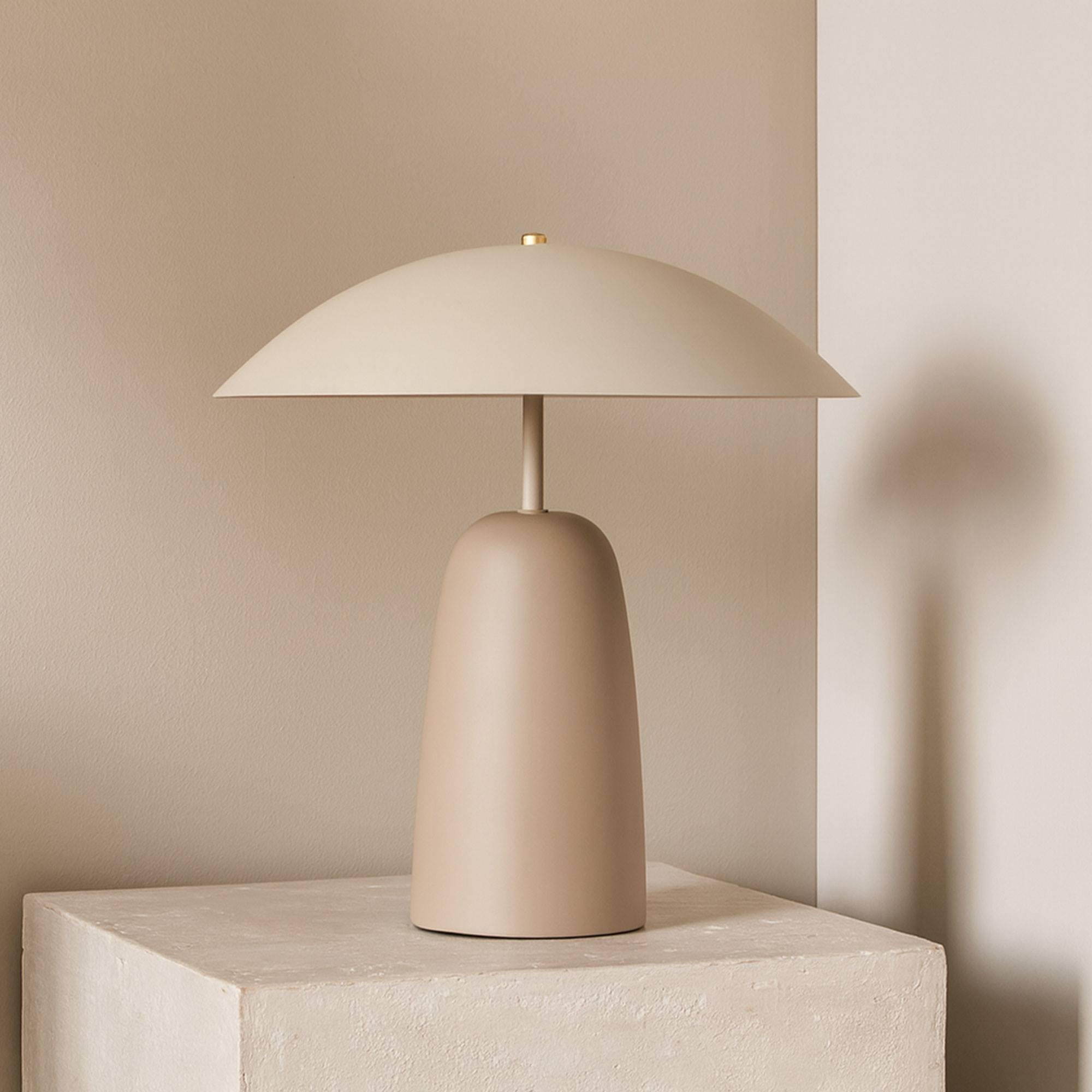 Una lámpara beige con pantalla curva sobre un bloque de piedra. Sombra de la lámpara en la pared.