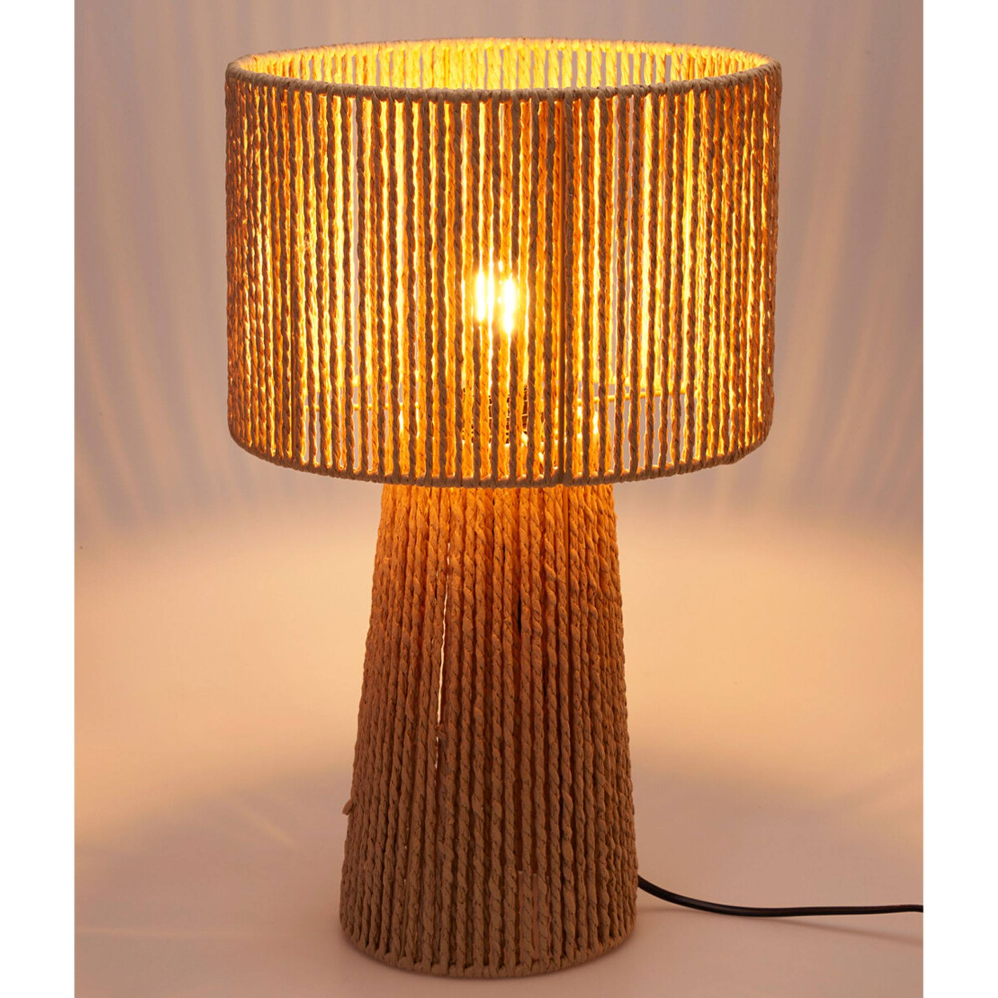 Una lámpara de cuerda beige con pantalla y base cilíndricas, iluminada desde adentro, sobre fondo blanco. Se ve un cable negro.